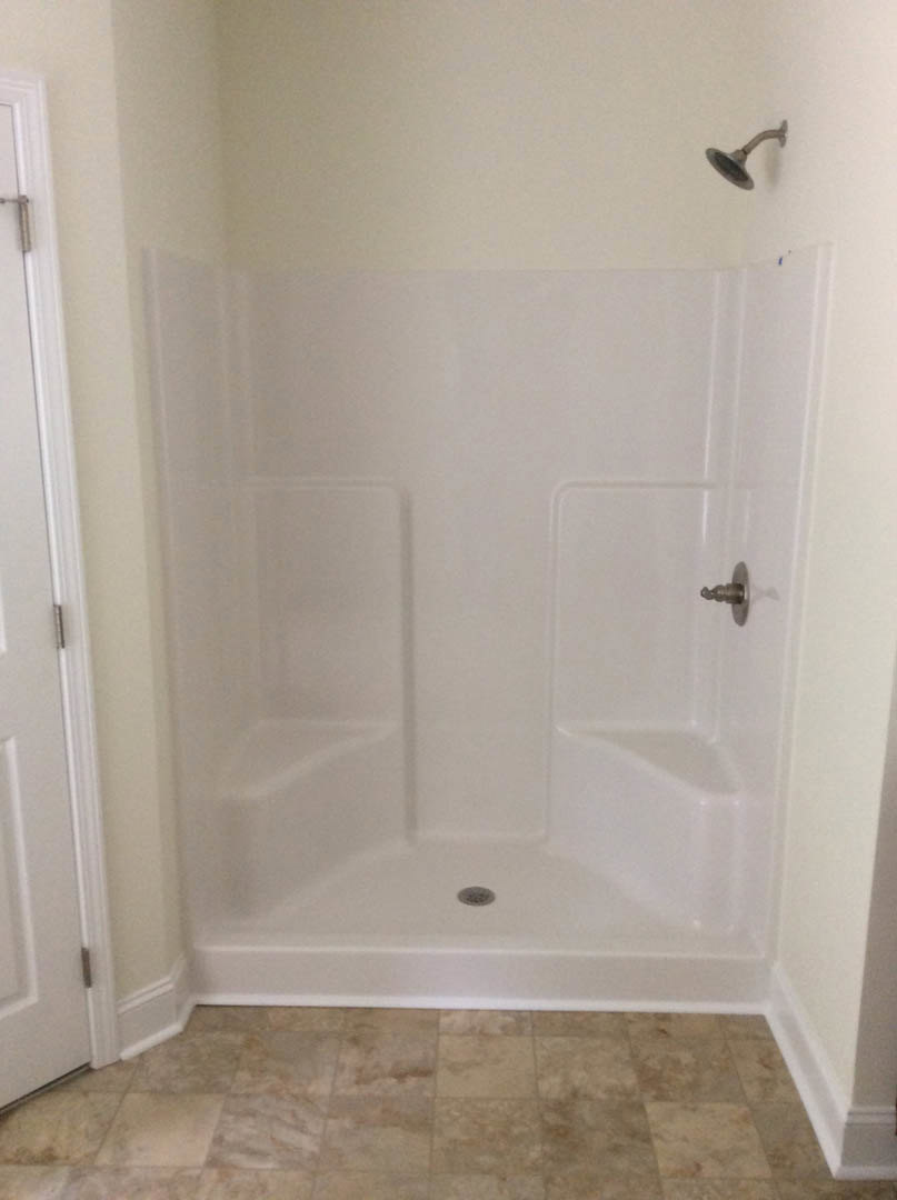 Glass shower enclosure with marble tile walls, chrome shower head, and open door revealing polished metal handle and textured tile floor