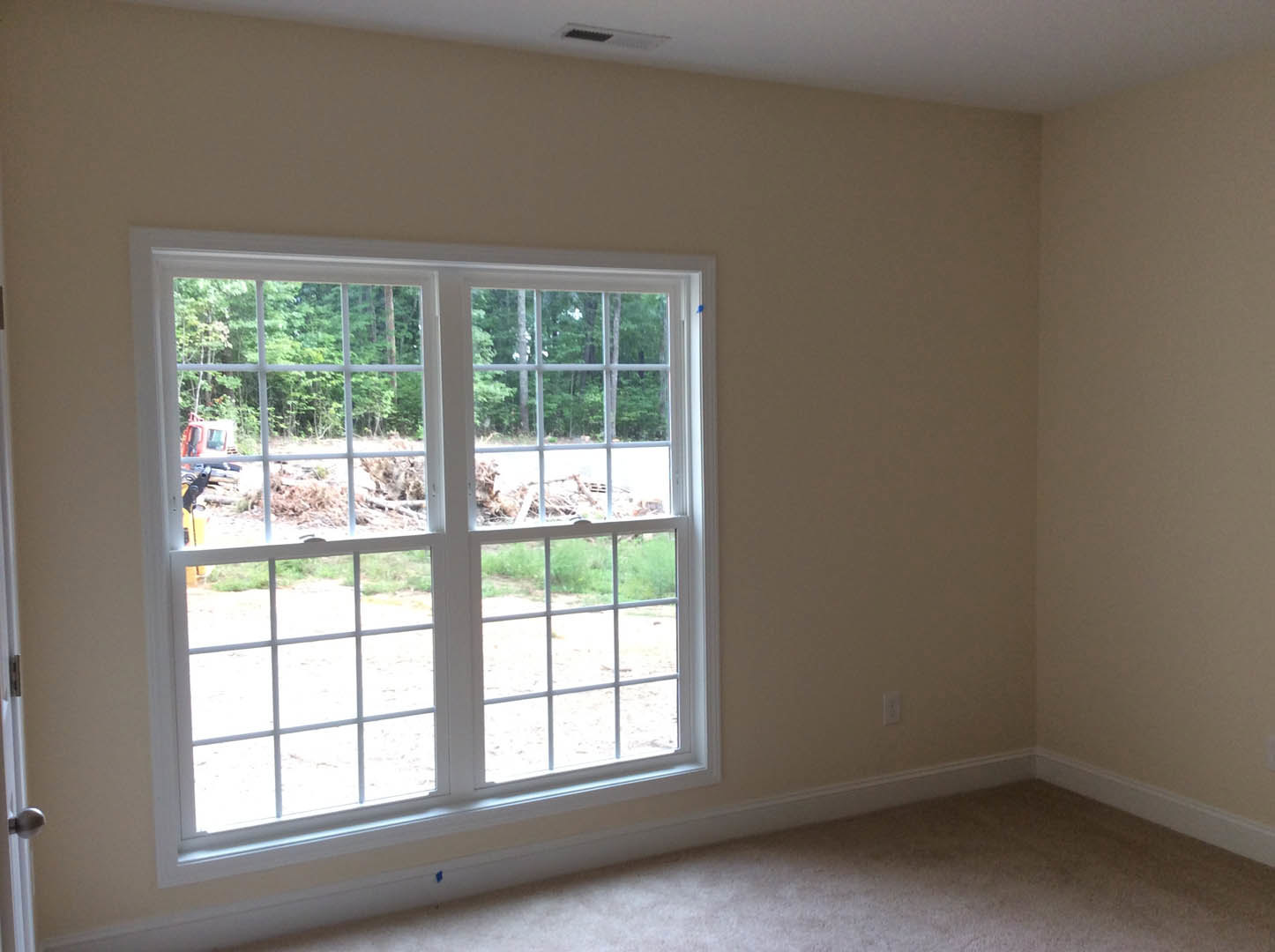 White carpeted floor and walls in a room with a large window featuring a white frame, overlooking trees and bare ground.