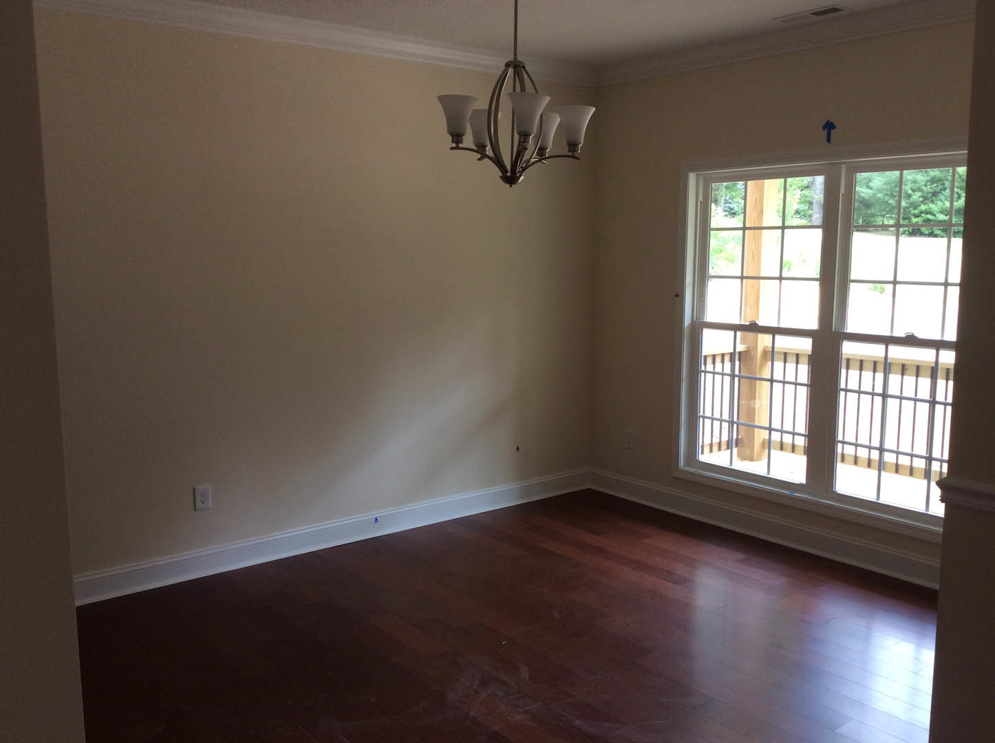 Wood flooring with white baseboard trim, large window with side bars, ornate chandelier hanging from ceiling, plaster walls