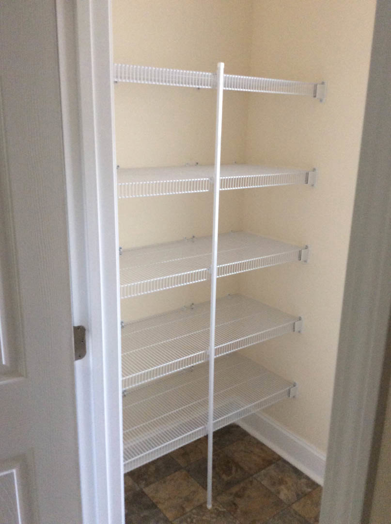 Walk-in closet with white built-in shelves, white walls, and light-colored tile flooring