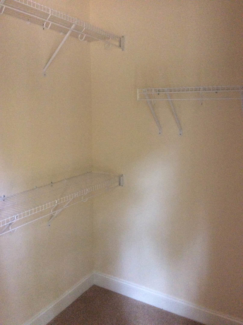 White plaster wall with built-in white metal shelves and hooks, light-colored ceiling and floor in a modern interior room.