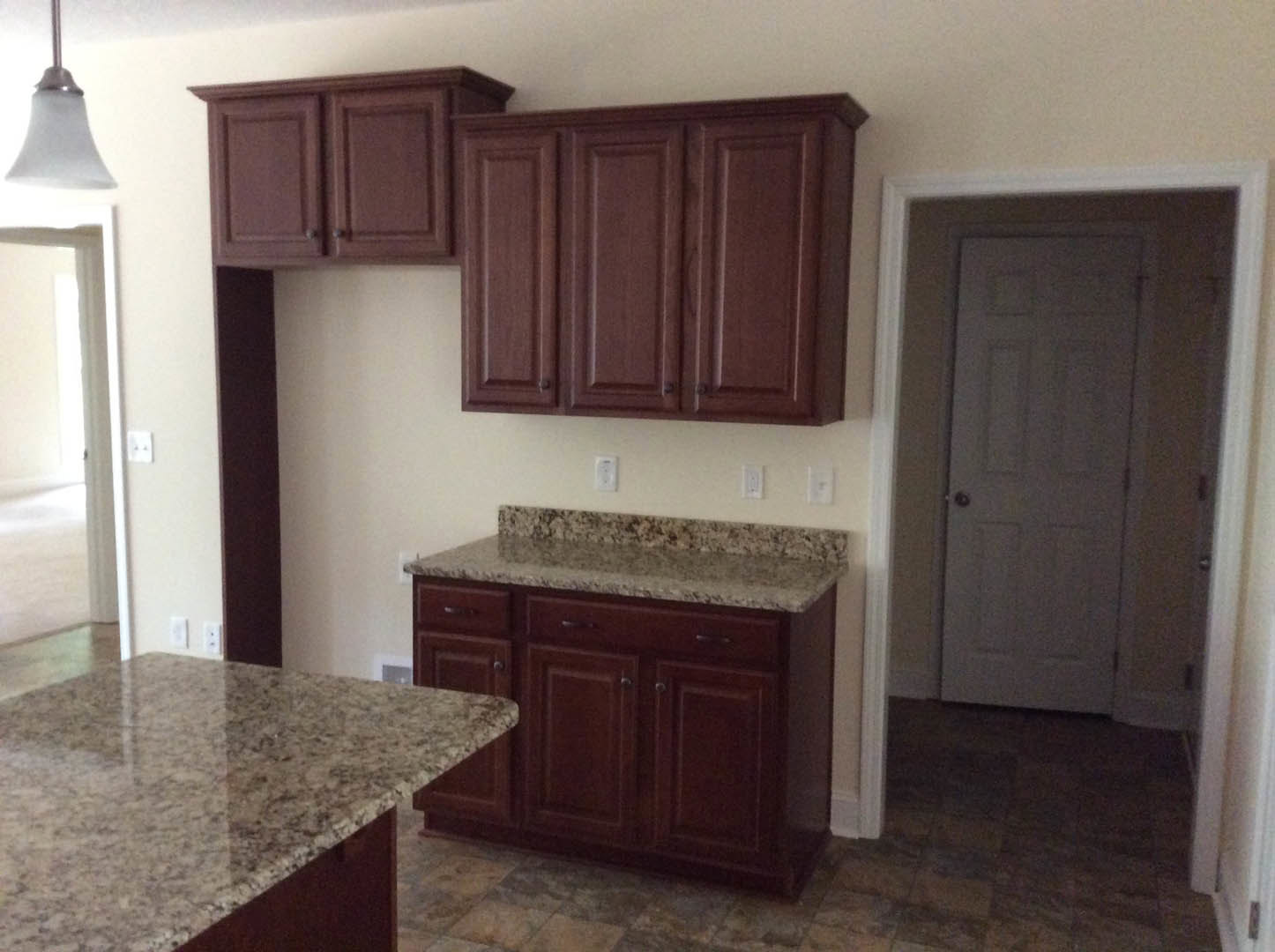 Granite countertops with marbled surface, wooden upper cabinets, tile backsplash, stainless steel sink, white door, and recessed lighting in a modern kitchen.