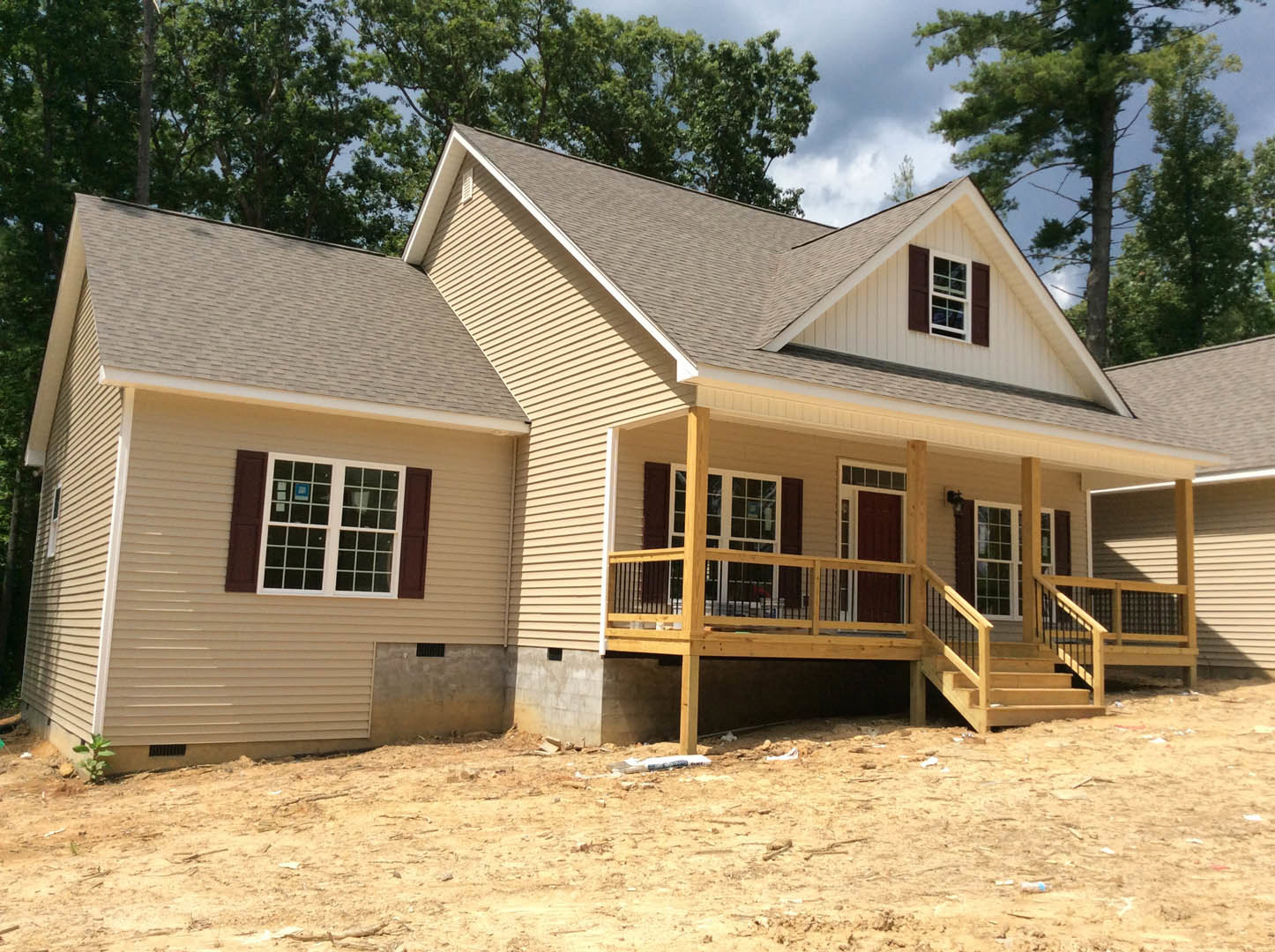 Two-story house with multi-pane windows, dark shutters, wood porch, and deck; dirt hill with scattered debris and a small plant growing near the foundation.