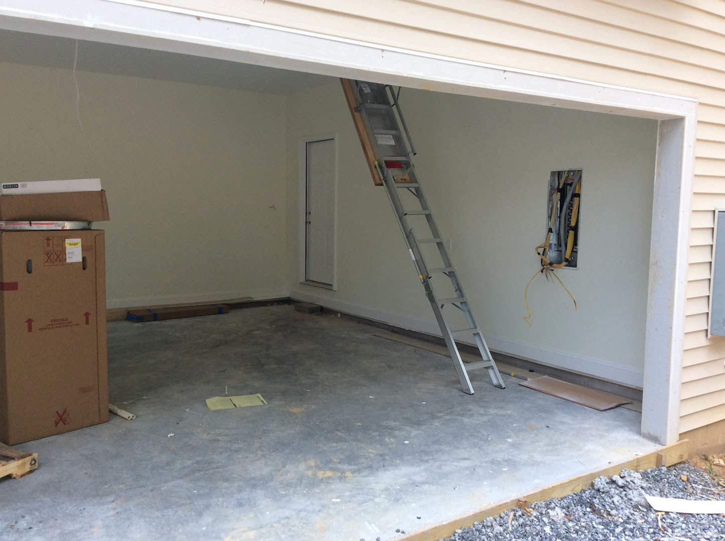 Ladder leaning against unfinished plaster wall, cardboard box with red arrows on concrete floor, white door with black handle, exposed metal frame, visible cable, white window