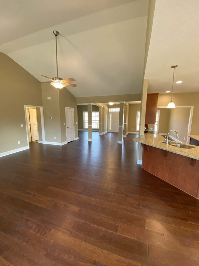 Spacious open floor plan featuring hardwood floors, central kitchen island with built-in sink, white ceiling with recessed lighting, ceiling fan, and adjacent doorway