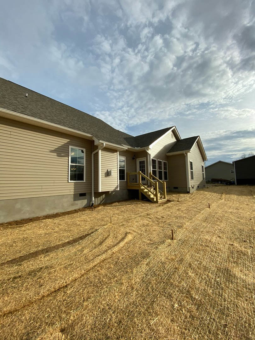 Two-story house with white-framed windows, wooden deck, and green grass yard under a cloudy sky