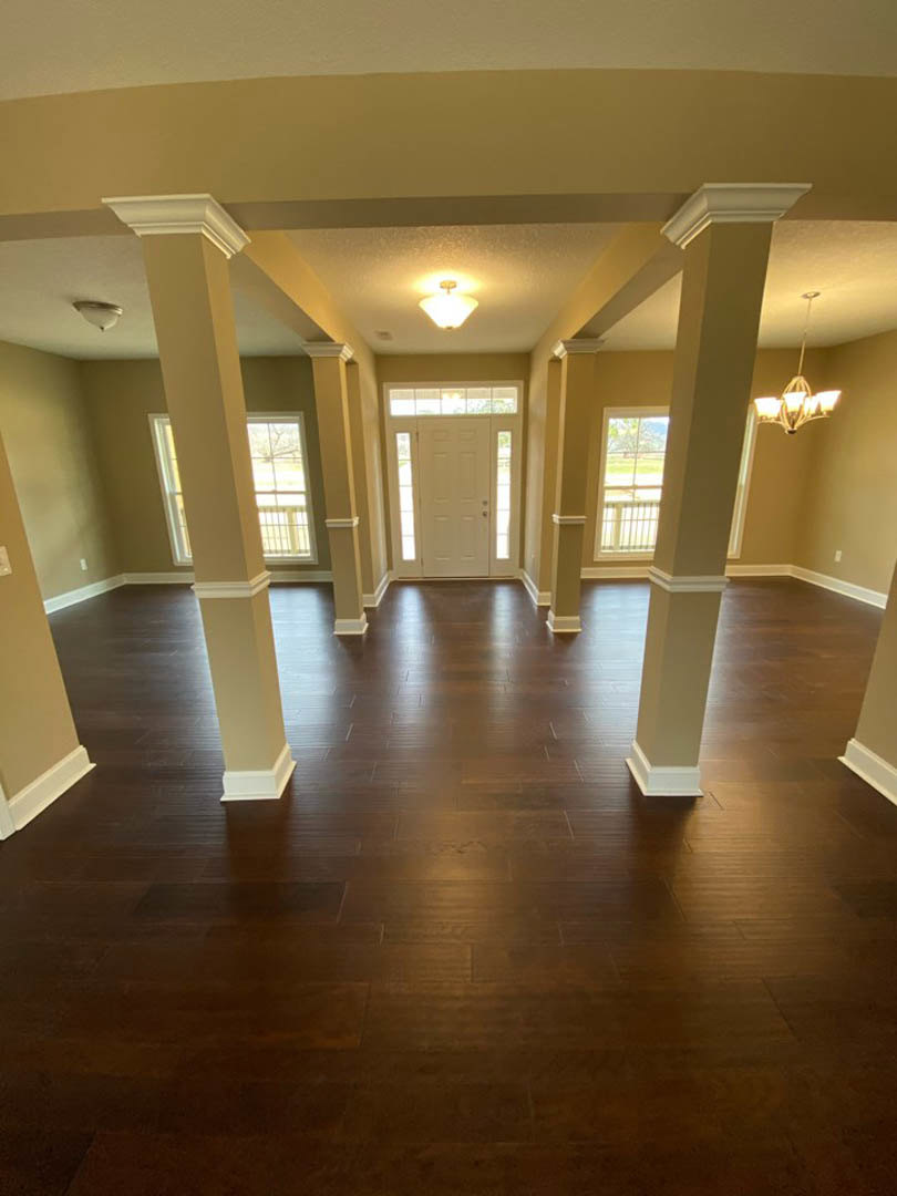 Open living space with white columns, hardwood floors, glass-paneled door, and chandelier hanging from a tray ceiling