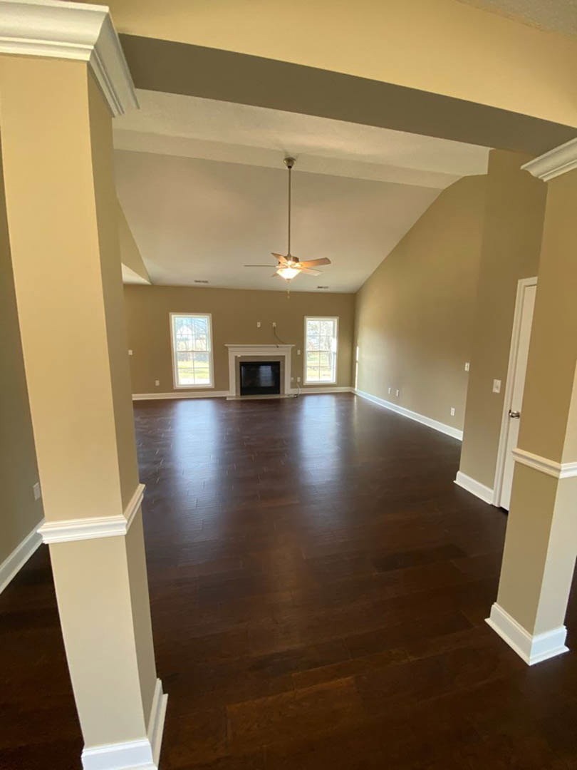 Living room with hardwood floors, white-framed fireplace, ceiling fan with light, white window trim, neutral walls, and decorative molding
