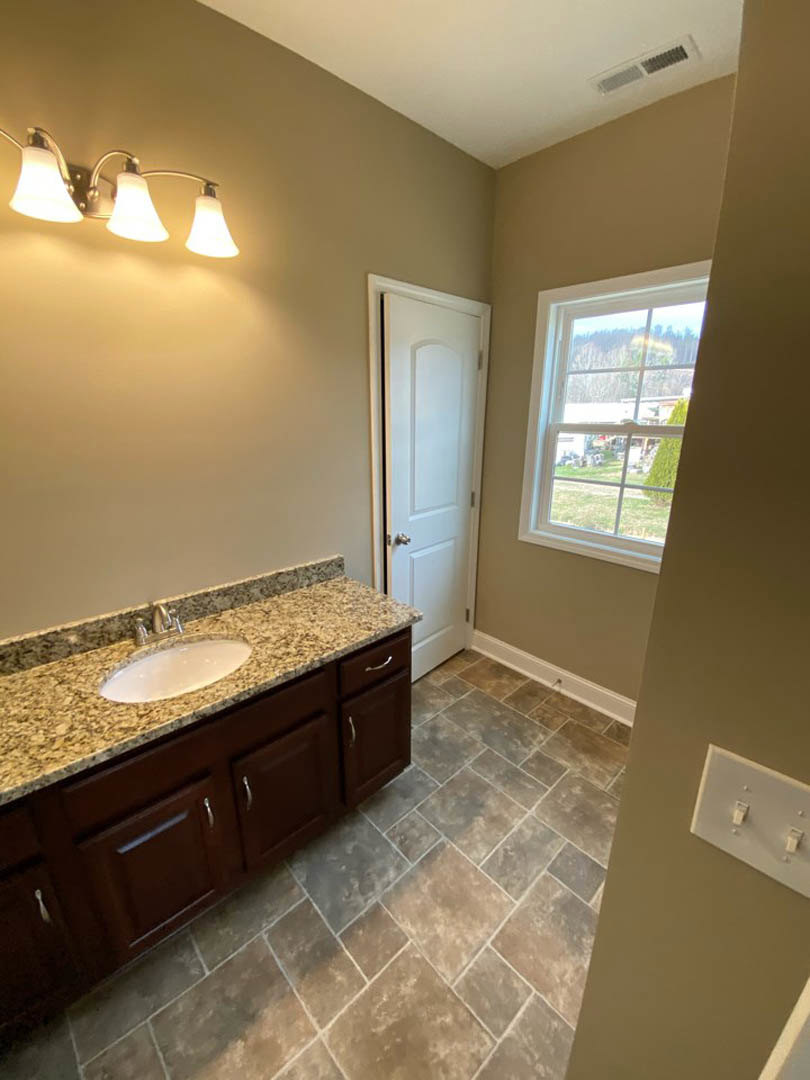 Bathroom with marble countertop, undermount sink, chrome faucet, white cabinetry, large window overlooking yard, white door, modern light fixture, and dual light switch on pale