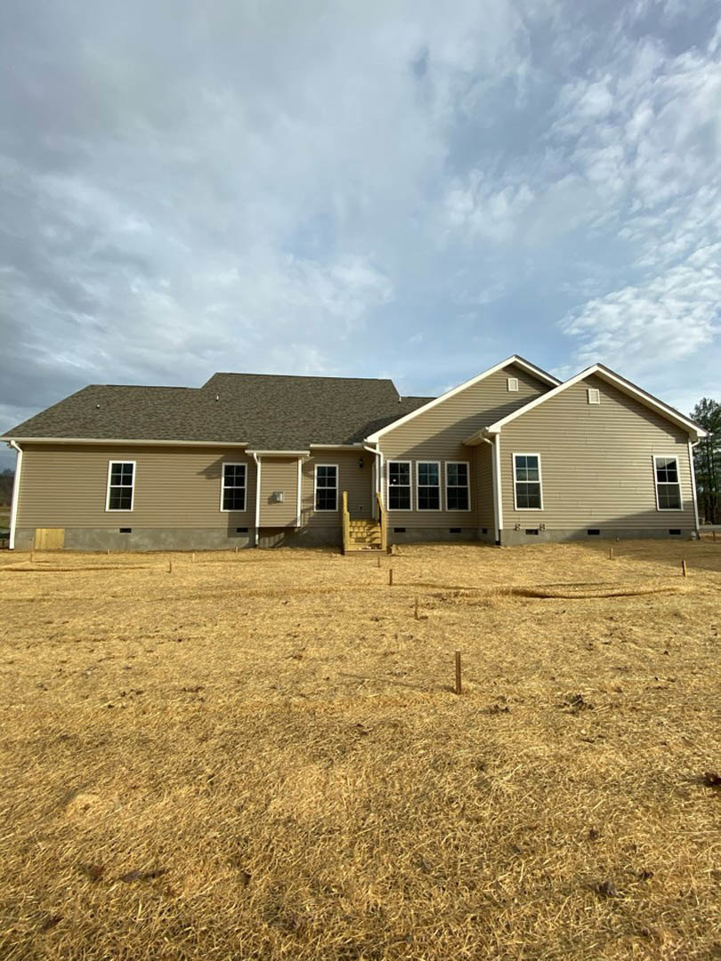 Modern two-story home with gray siding, gabled roof, several windows, expansive green lawn, and partly cloudy sky