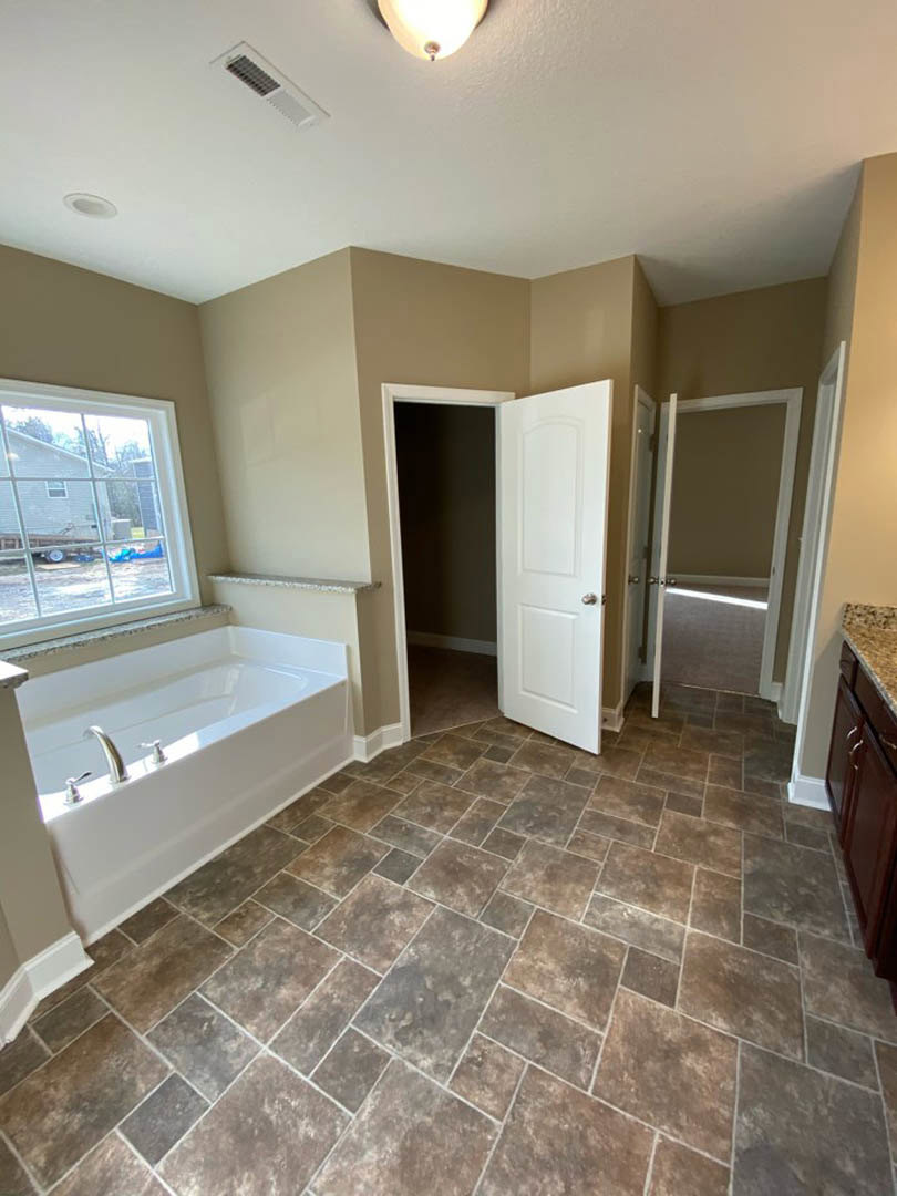 Bathroom with white tile floor, freestanding bathtub with chrome faucets, single sink vanity, wall mirror, window showing trailer outside, white door with silver handle