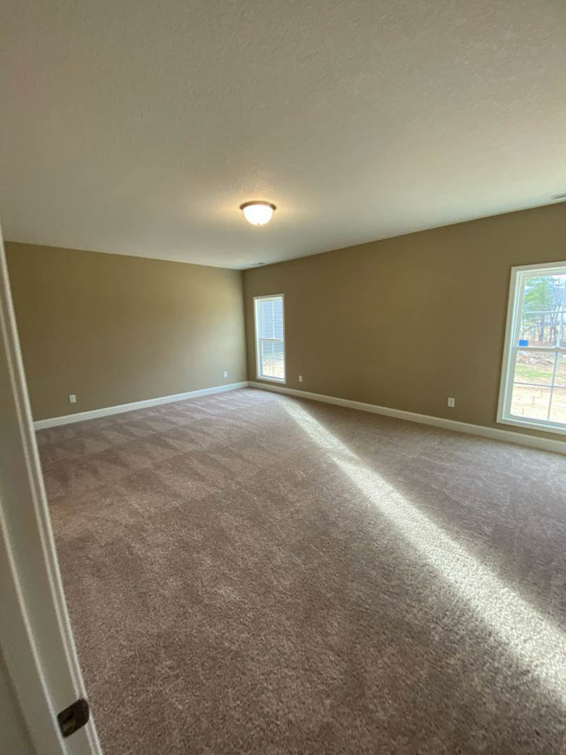 Neutral-toned carpeted room with multiple windows, one featuring a blue sticker and another with closed blinds, white plaster walls, ceiling-mounted light fixture