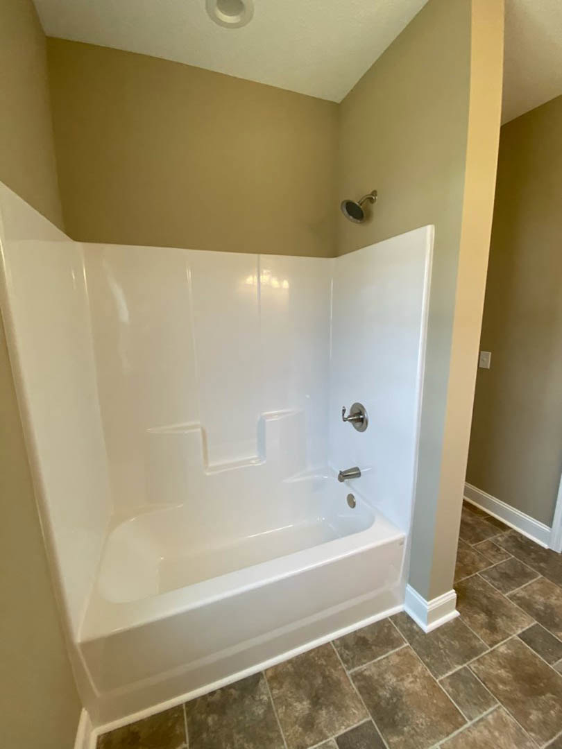 Freestanding white bathtub with chrome faucet, textured tile floor, plaster walls, wall-mounted shower head, and modern sconce lighting in a contemporary bathroom