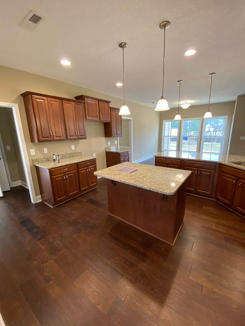 Kitchen with light wood cabinets, matching wood flooring, marble countertop, white walls, black cabinet handles, and a window above the sink.