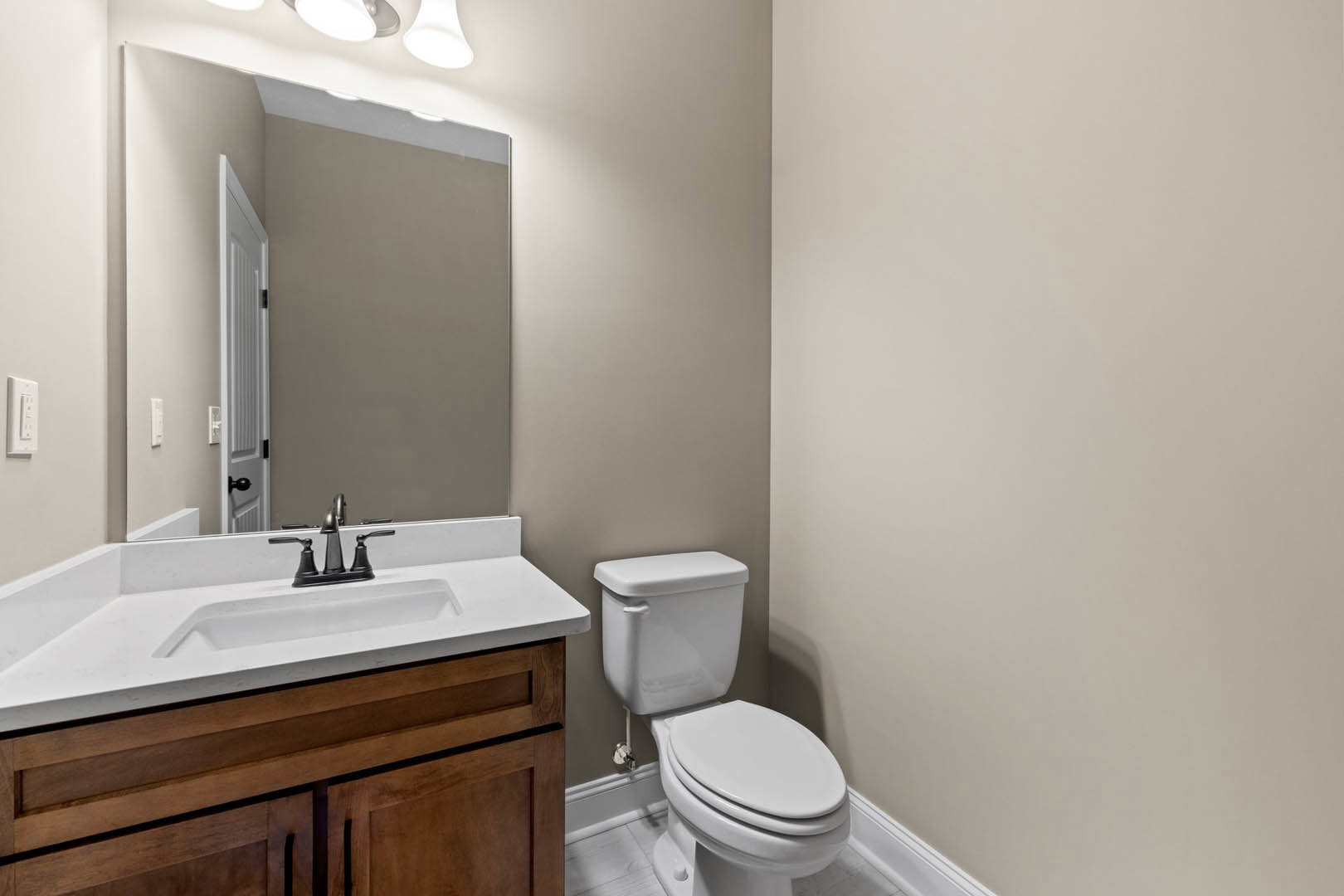 White bathroom with tile walls, modern toilet, rectangular sink with chrome faucet, and white door featuring black handle