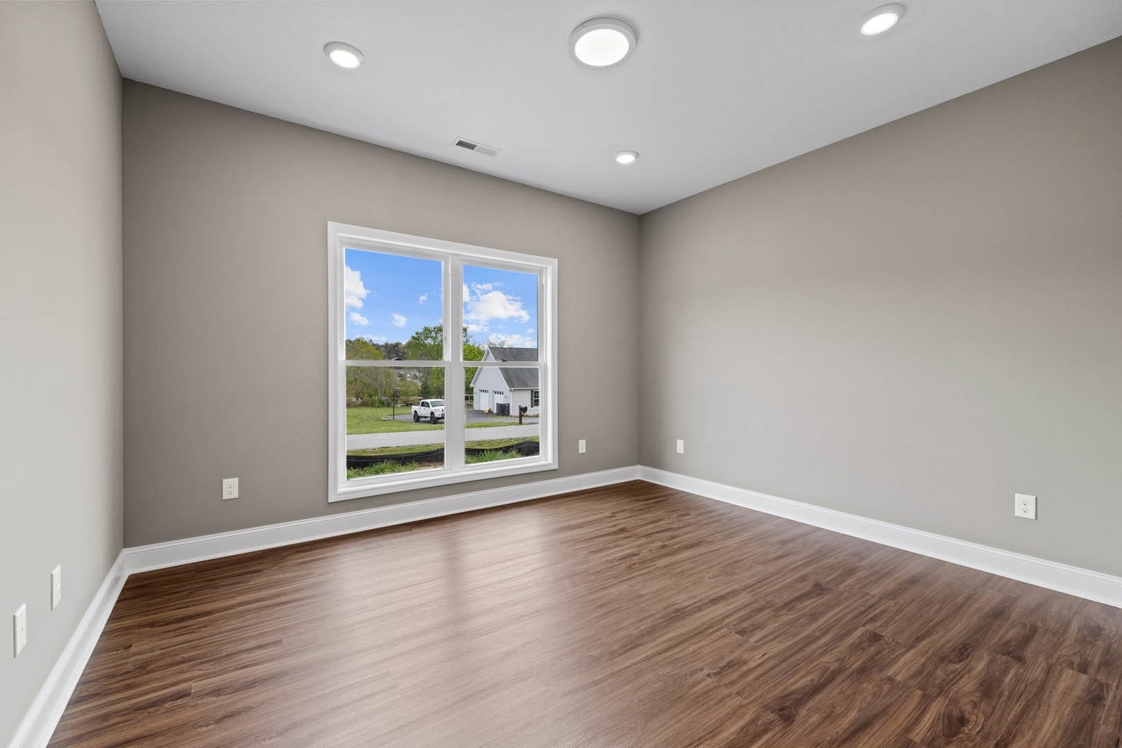 Bright room with wide window, natural hardwood flooring, white walls, recessed ceiling lights, and circular light fixture