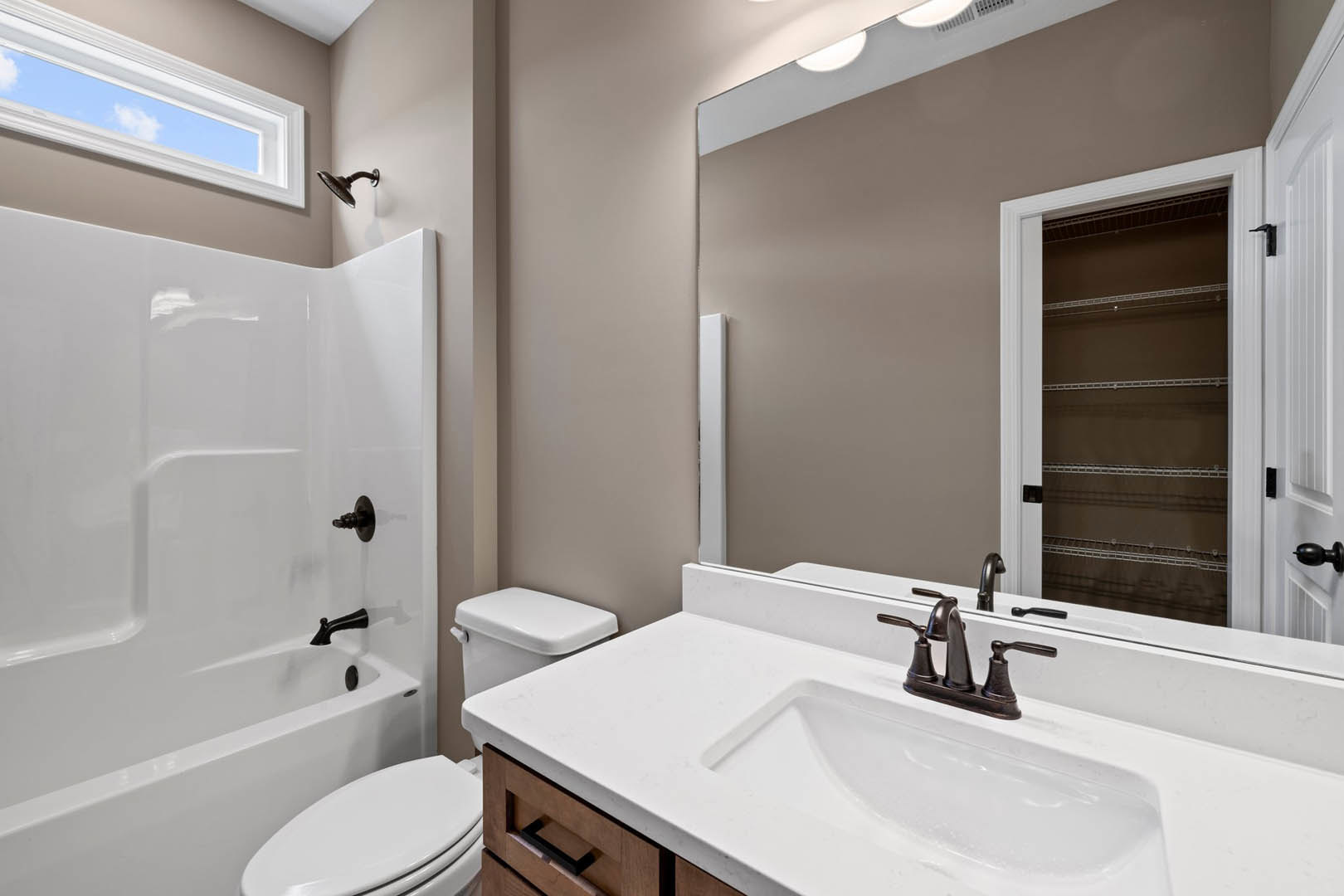 Modern bathroom featuring a white bathtub with matte black faucets, white sink with black hardware, wall-mounted mirror, tiled walls, and a glass-enclosed shower with a black