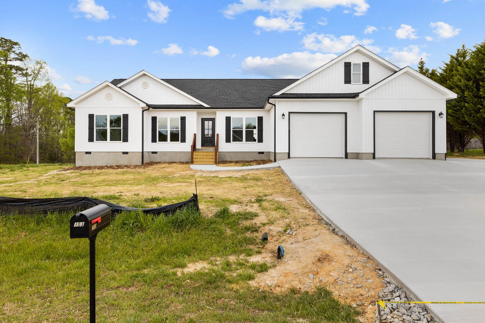 Modern two-story home with white siding and black trim, concrete driveway bordered by rocks and a yellow line, white garage door, manicured lawn, and black signpost near the