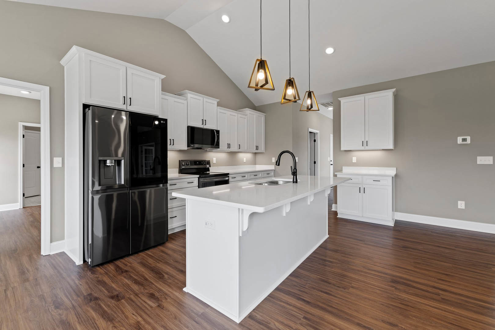 White kitchen with black refrigerator, white cabinets with black handles, white island, black pendant lamp, and geometric ceiling light fixture.