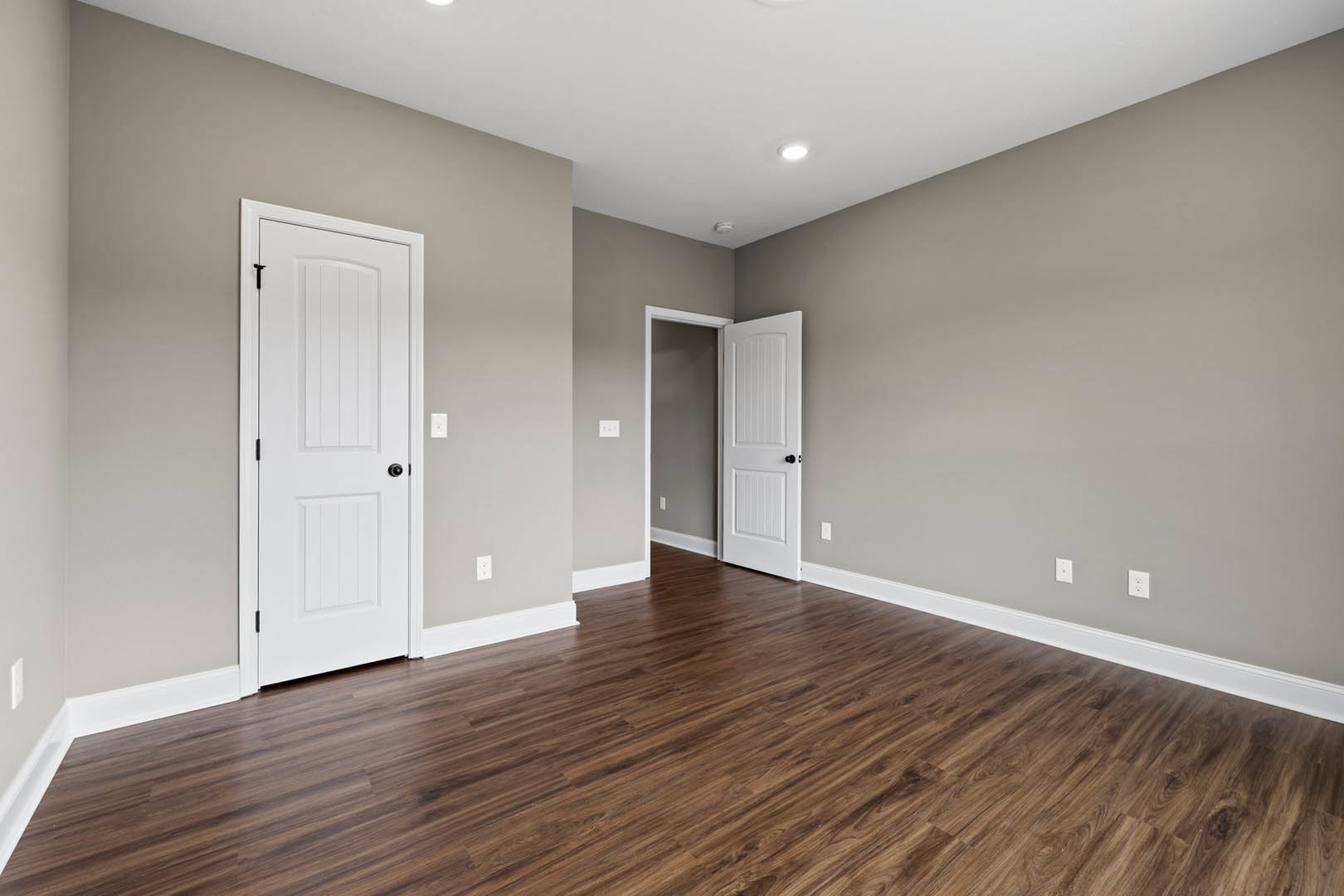 White paneled doors with black knobs, dark wood flooring, white door frames, and a white ceiling with recessed lighting.