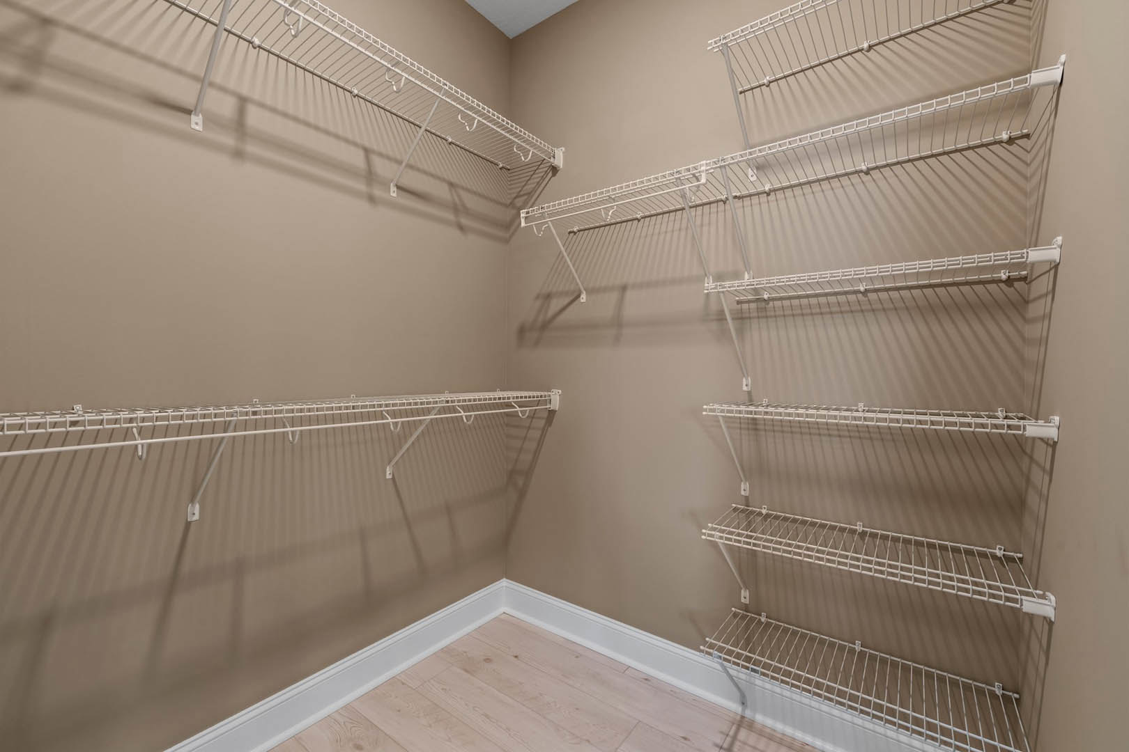 Wood plank flooring with white baseboards, built-in white wire shelving mounted on plaster wall in a residential interior room.