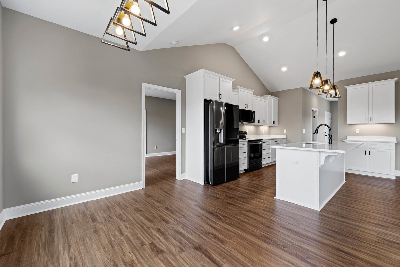 Open kitchen and dining area with wood flooring, white cabinets with black handles, black refrigerator, white kitchen island, and modern light fixture