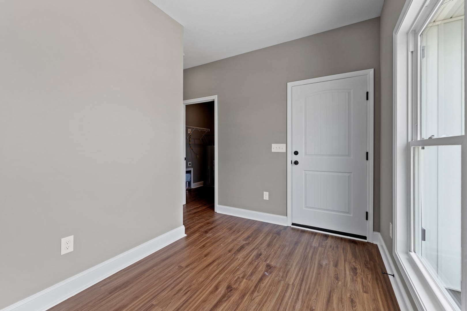 White walls and trim, wood flooring, white door with black handles, close-up window with white frame, electrical outlet visible.