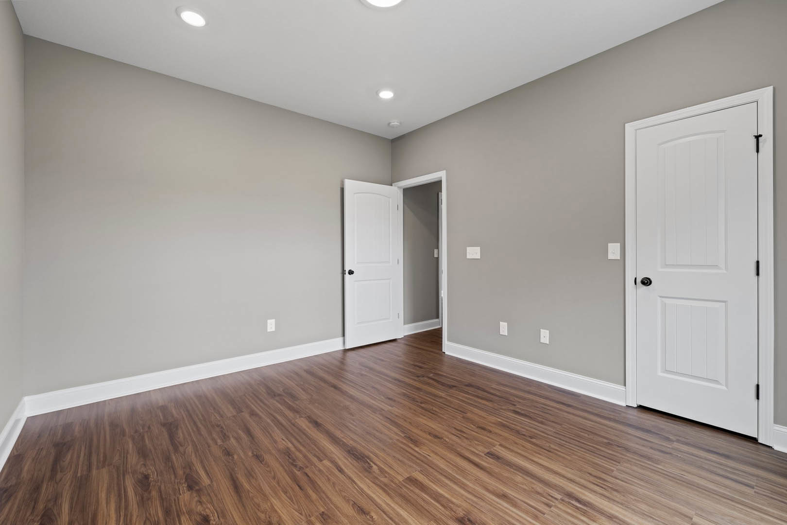 Open white door with black knob, wood flooring with white base trim, white ceiling featuring recessed lights