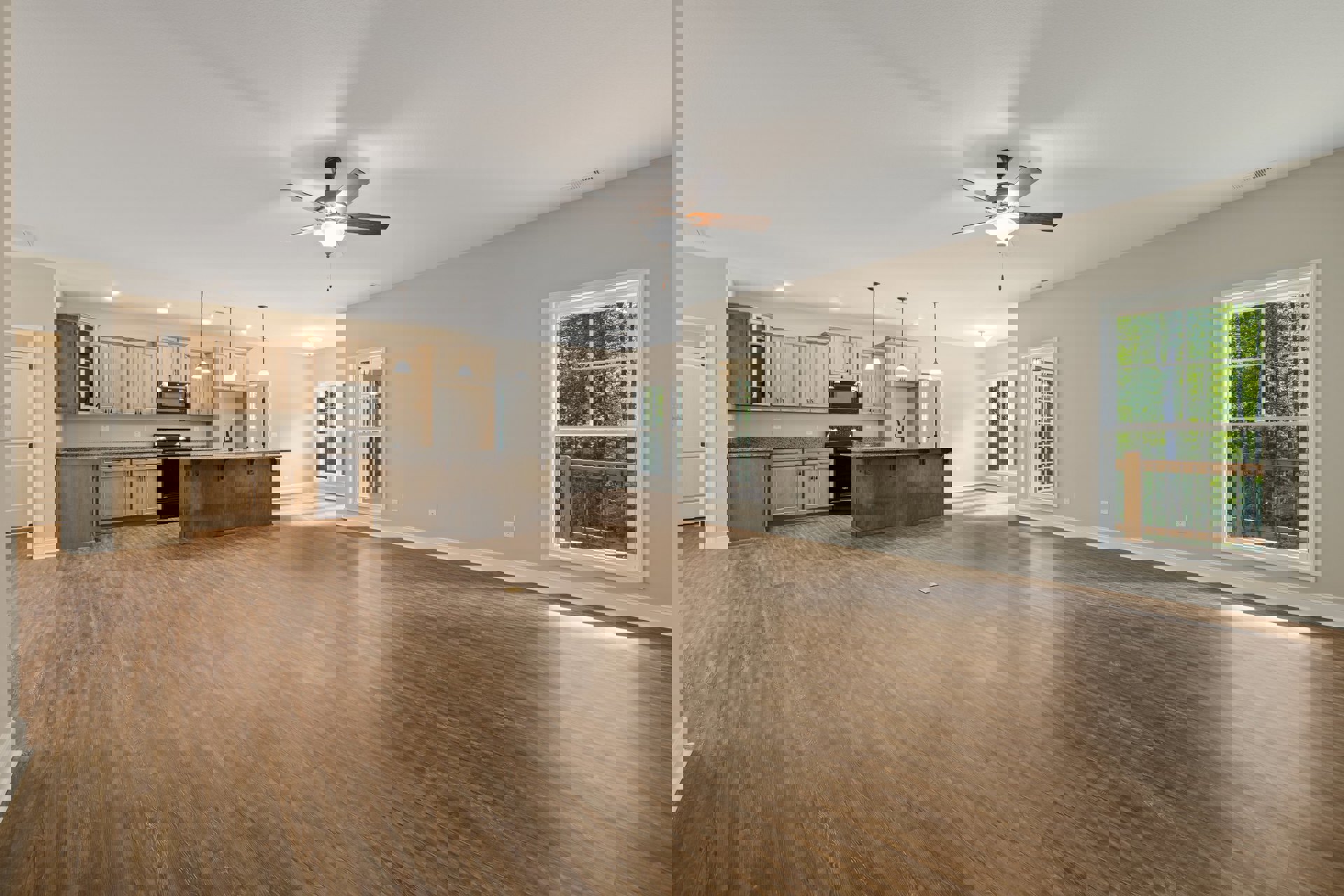 Open floor plan featuring wood flooring, spacious kitchen with black oven and large island, ceiling fan with light fixture, wooden railing with metal bars, and windows overlooking