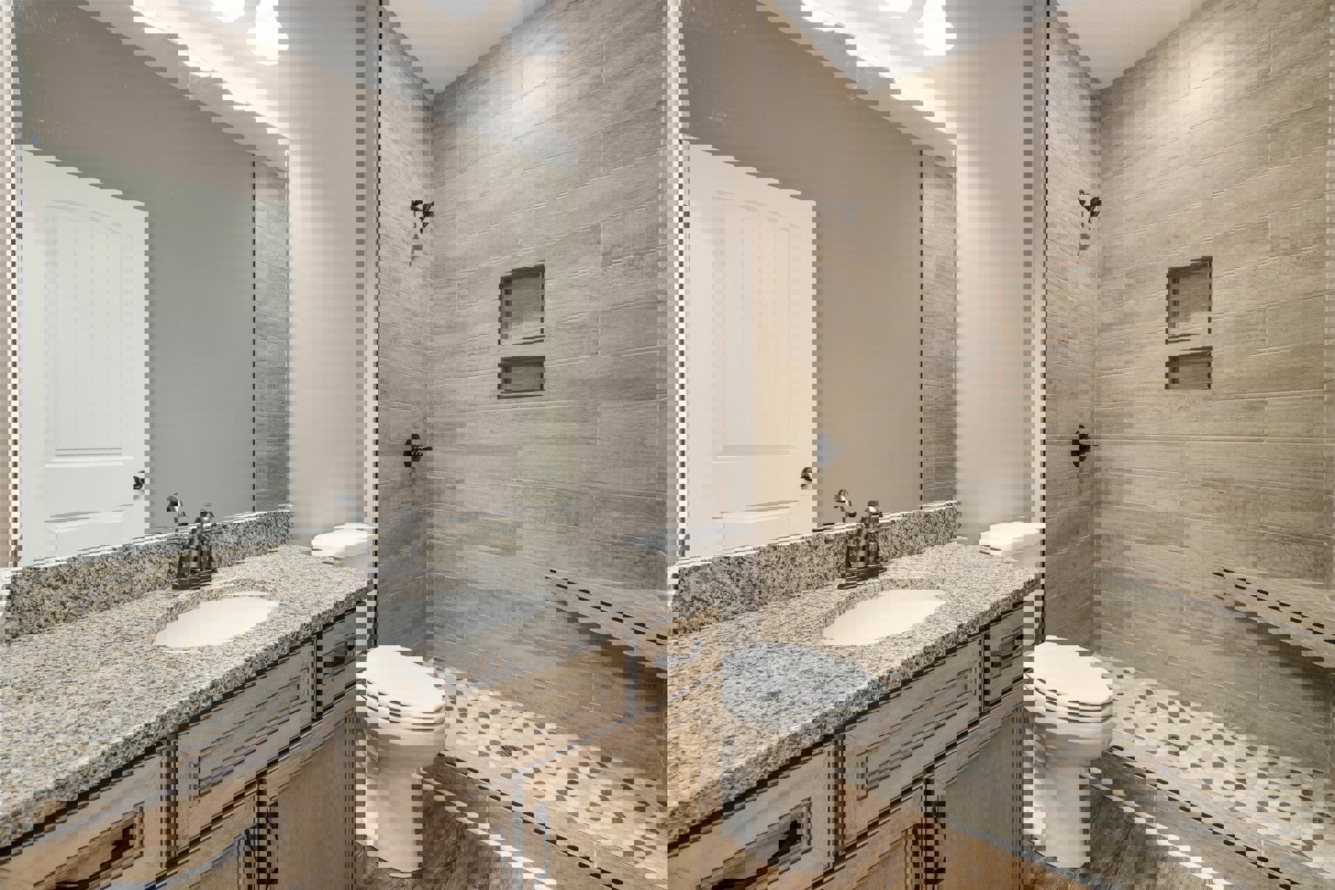 Marble countertop with undermount sink, glass-enclosed shower, white cabinetry, closed toilet, white door with black hardware, large wall mirror