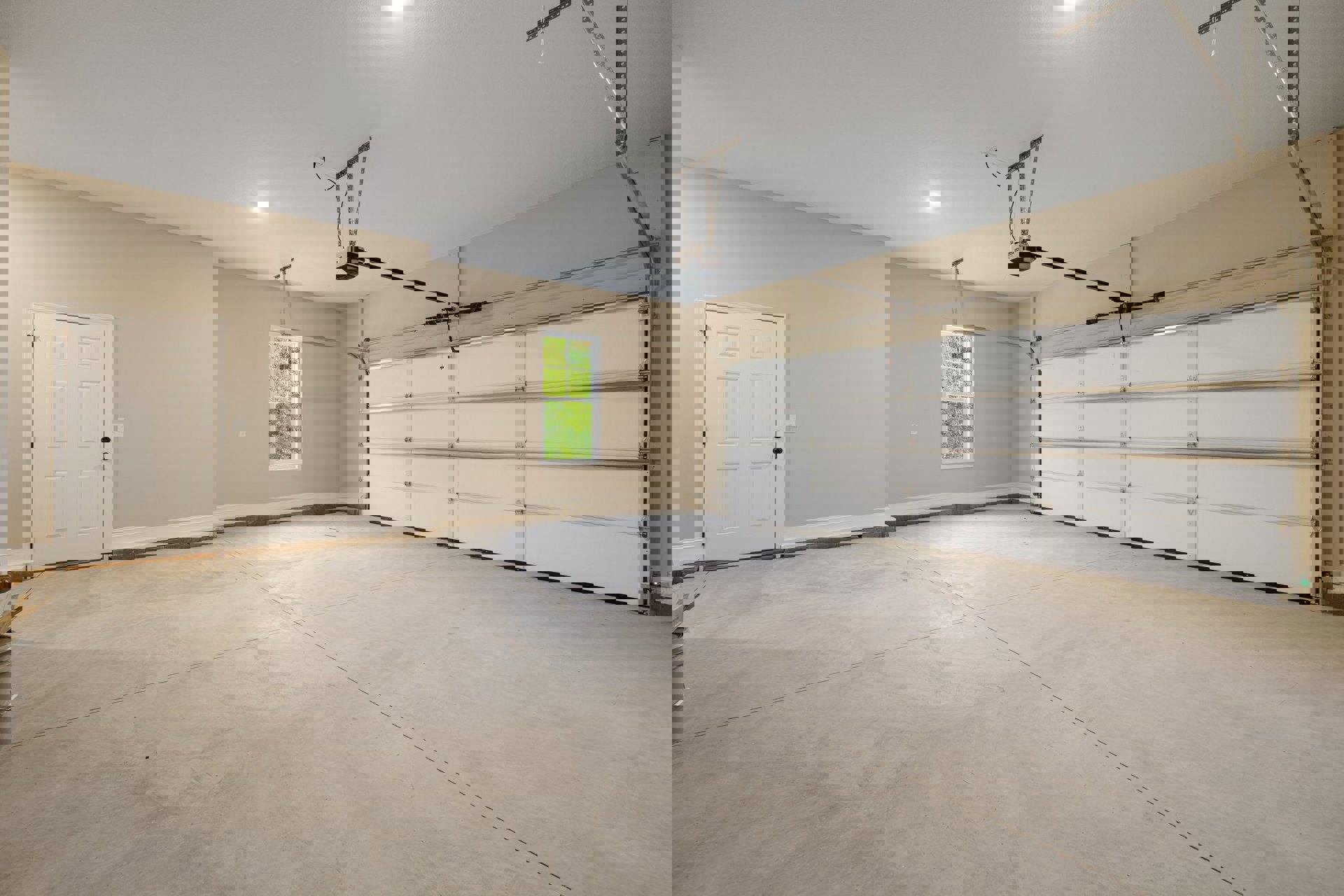 Spacious garage interior featuring a white paneled door with black handle, white plaster walls, concrete floor, ceiling-mounted light fixture, and window with white frame.