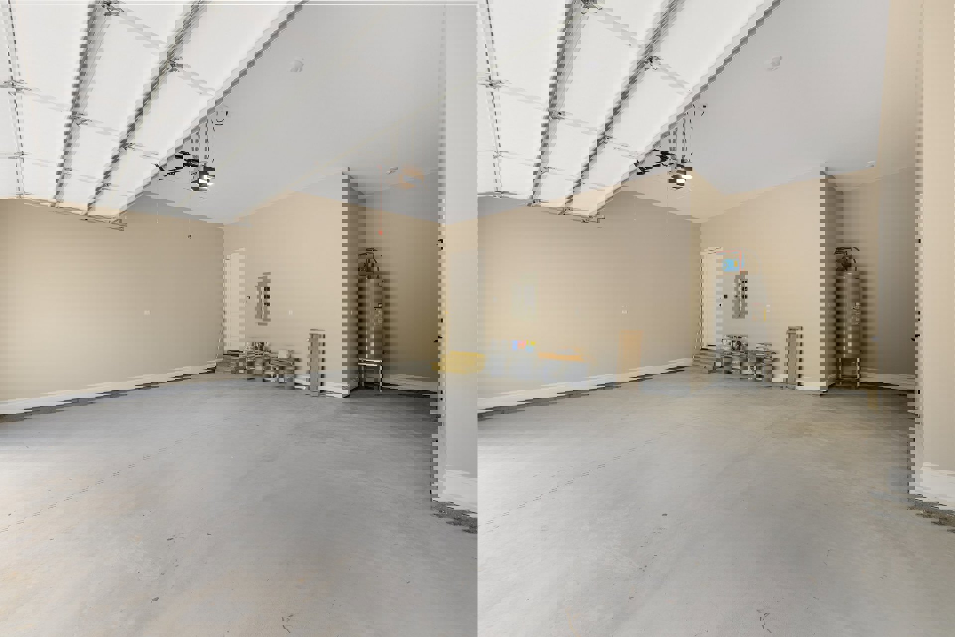 Spacious empty garage with smooth plaster walls, concrete flooring, overhead light fixture, white entry door with black handle, water heater with yellow label, and storage area