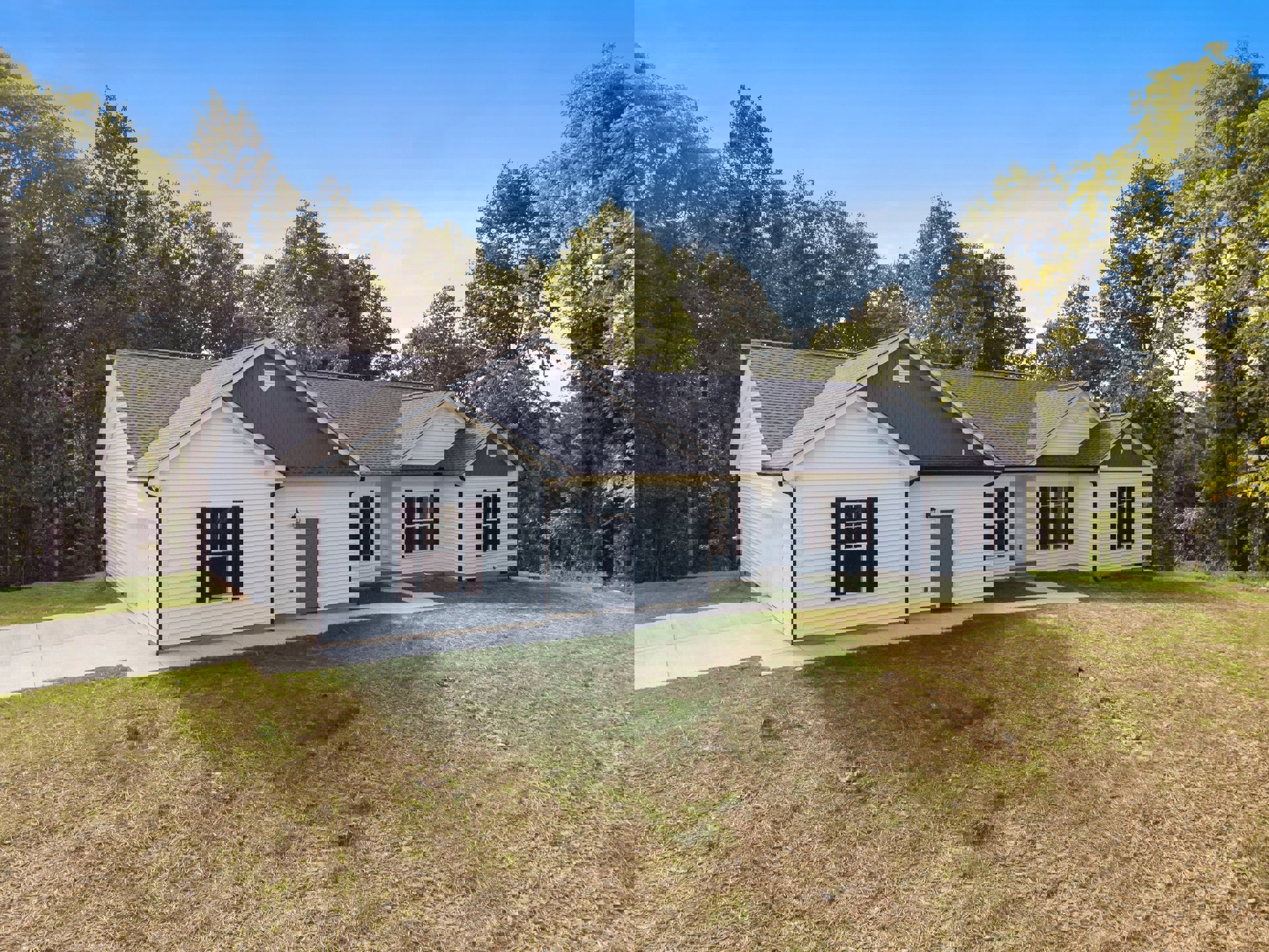 White house with gray roof and black shuttered windows, surrounded by green lawn and mature trees under a blue sky with scattered clouds