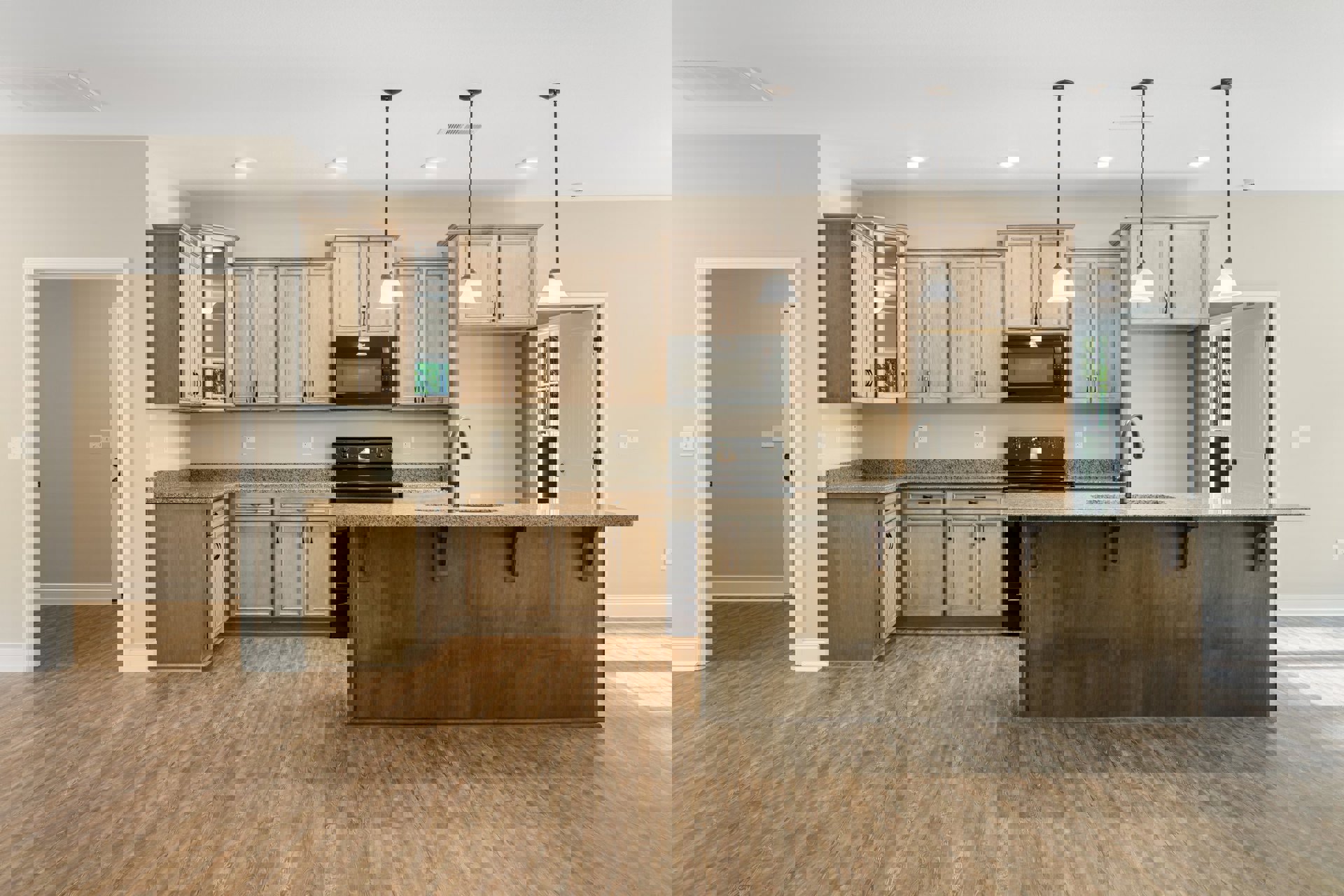 Spacious kitchen featuring a large central island, black microwave beneath overhead lighting, wood flooring, white countertops with built-in sink, and cabinetry along the walls.