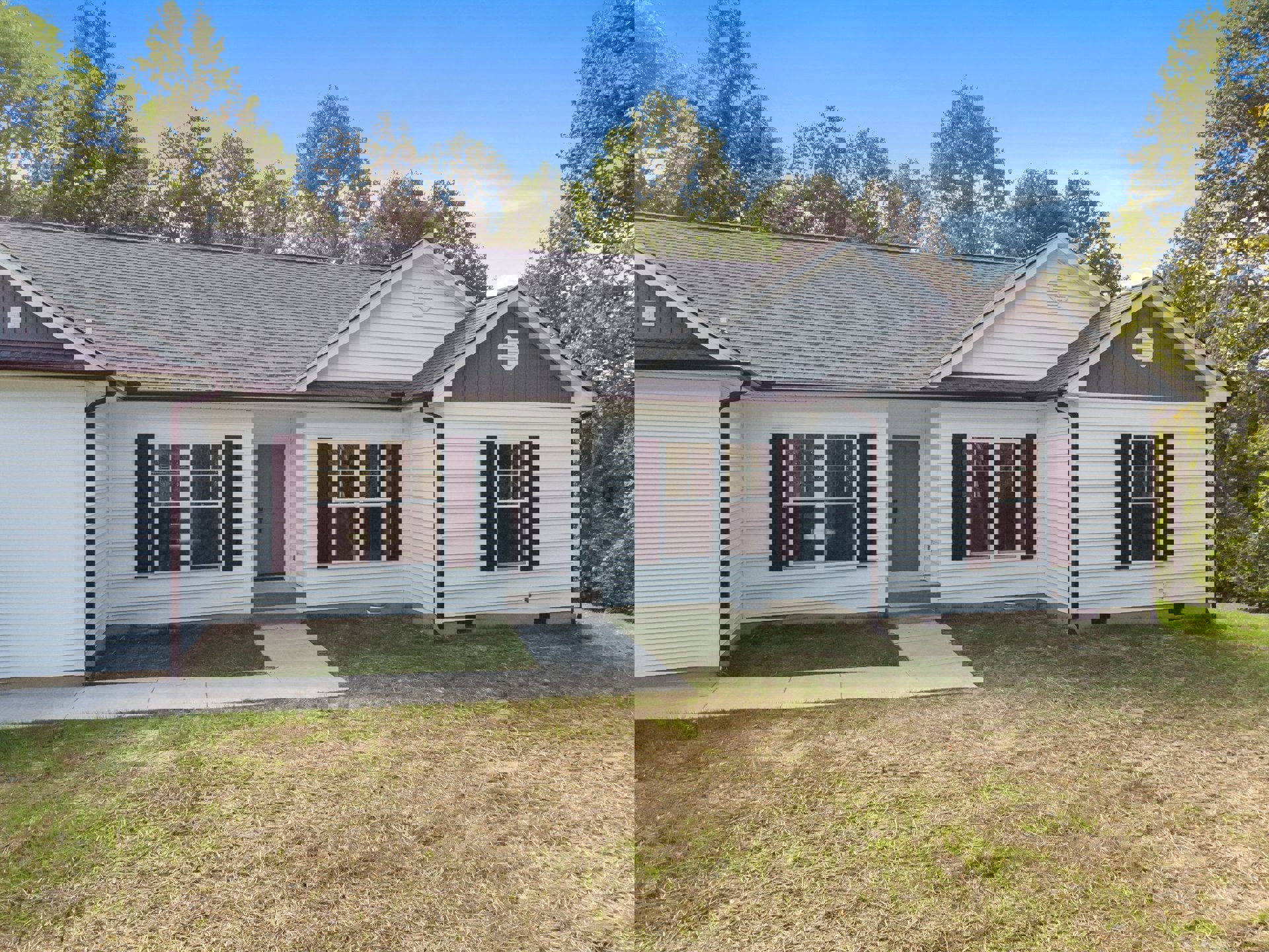 White house with black shutters, white trim windows, white front door, concrete walkway across green lawn, mature trees in background