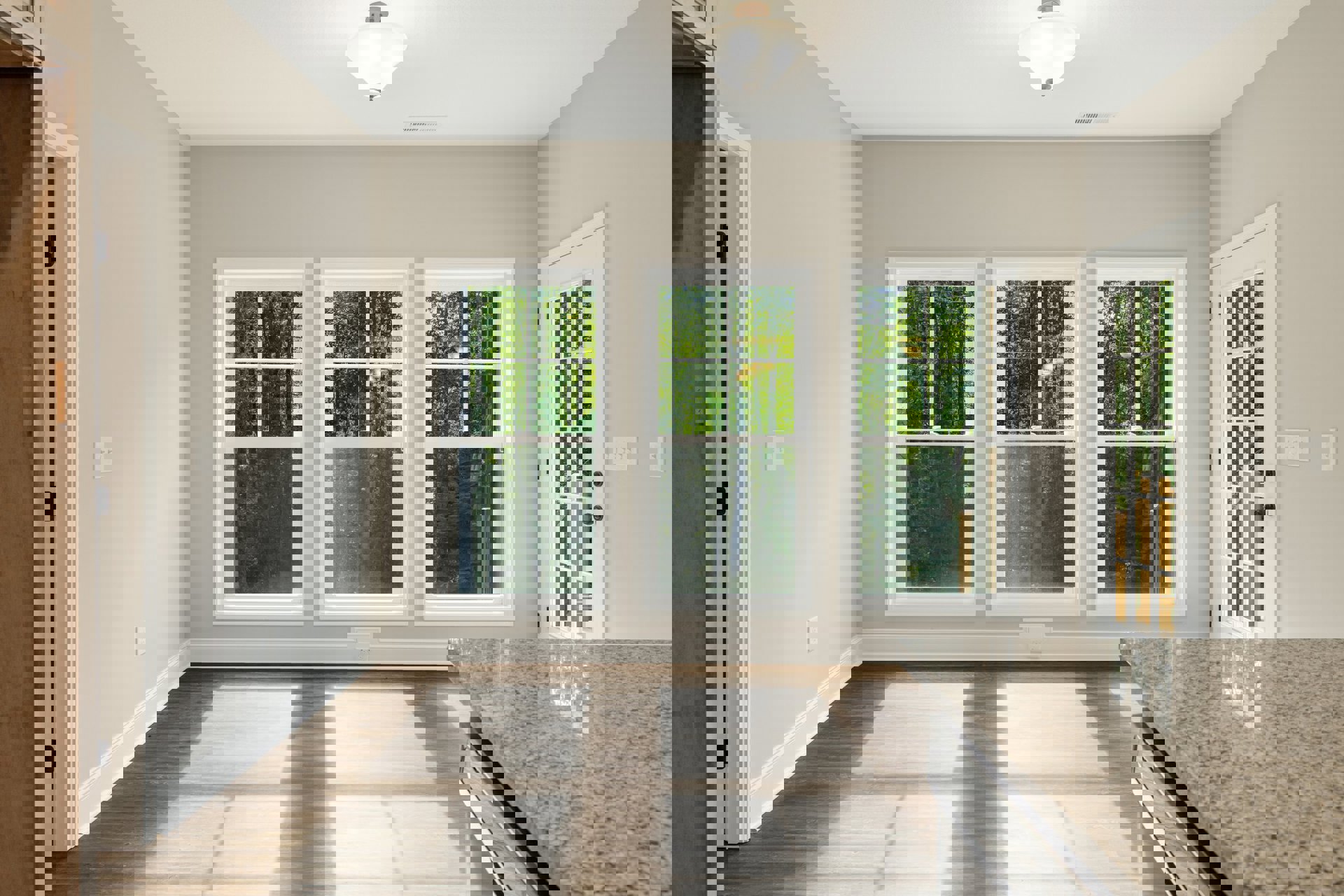 Marble kitchen countertop with wooden flooring, large windows overlooking trees, modern ceiling light fixture