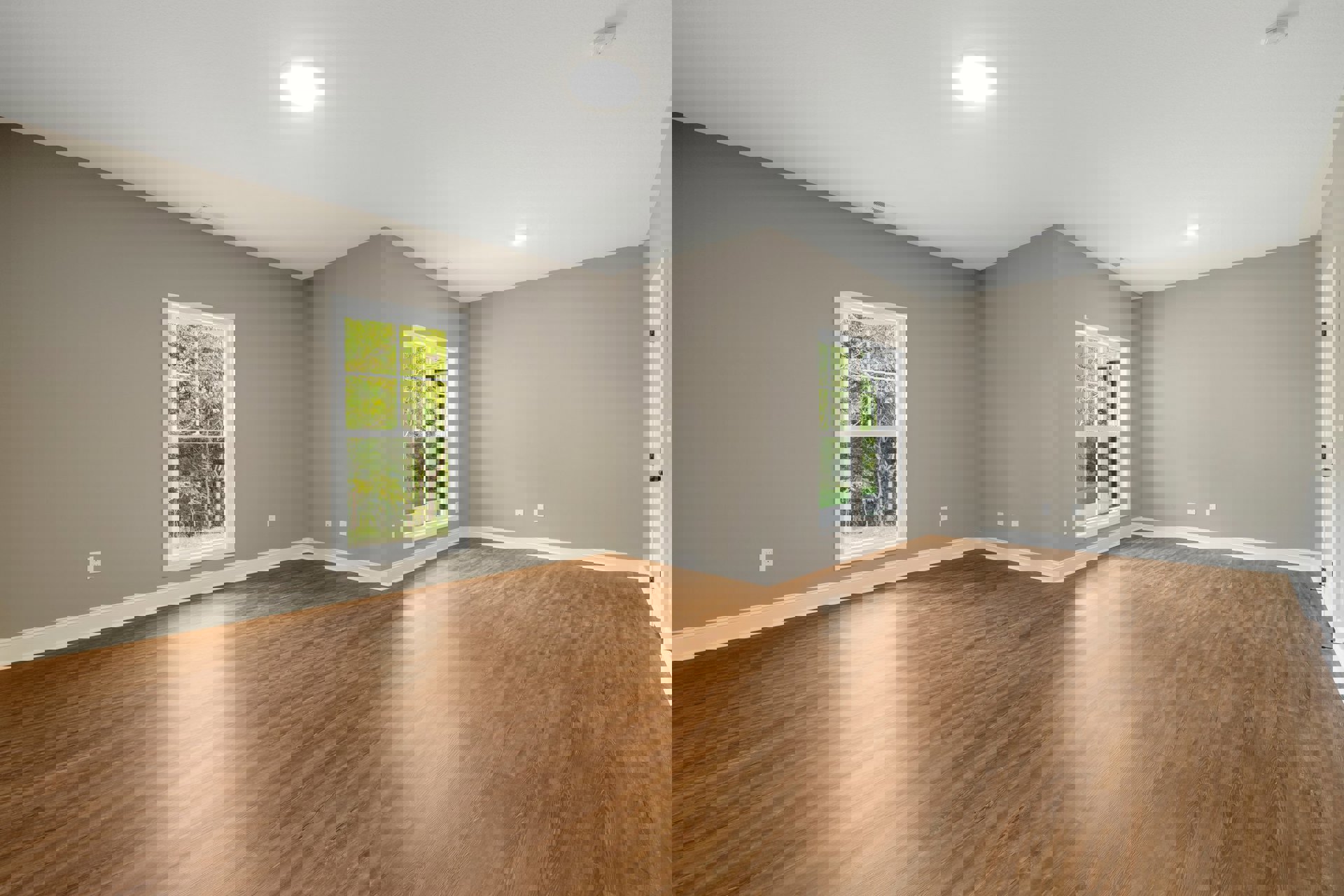 Room with hardwood flooring, large windows framed in white, ceiling light fixture, and view of trees outside