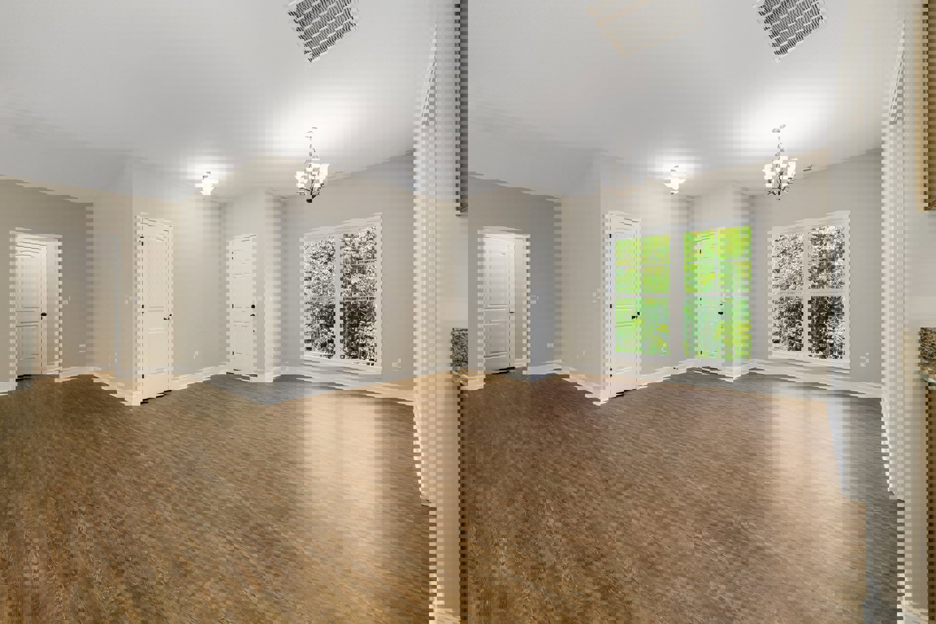 Wood floor room with white walls, white trim, two white doors featuring black knobs, ceiling vent, and window overlooking trees.