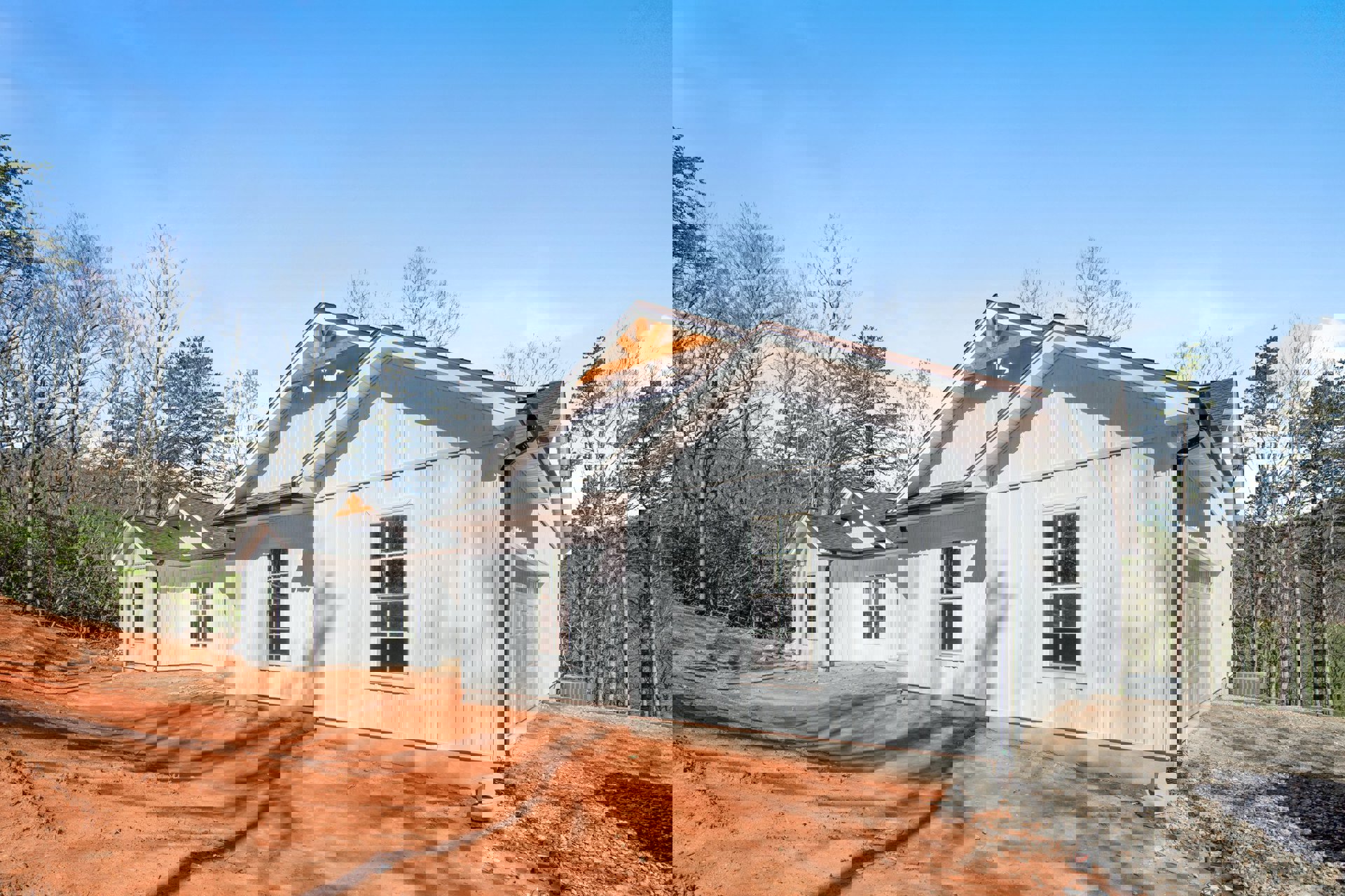 White siding house with attached garage, paved driveway, white-framed windows, gabled roof, leafless trees in front yard, cloudy sky overhead