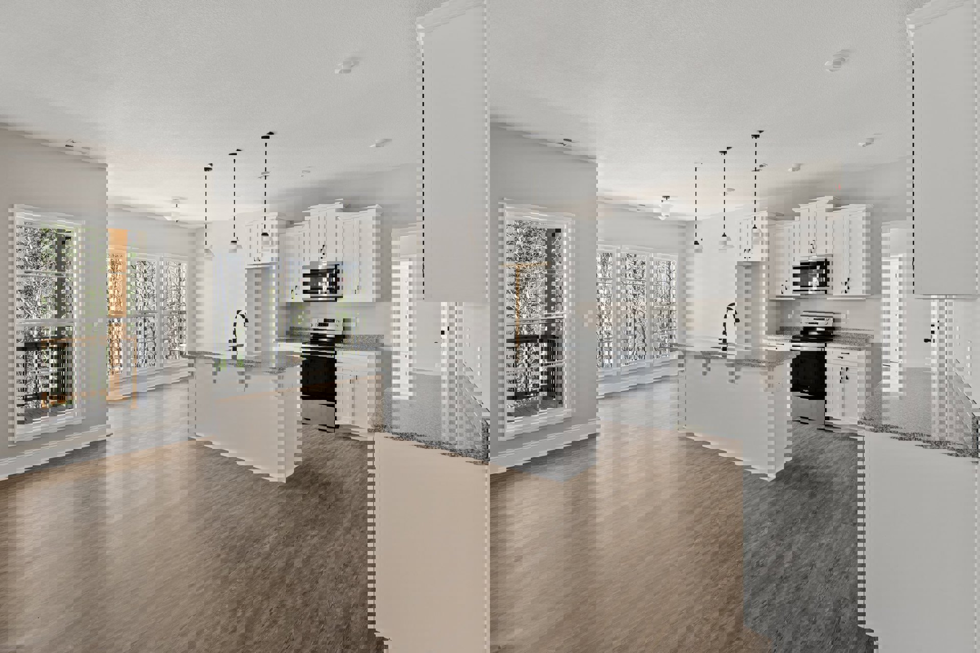 Kitchen and dining area with white cabinets, wood flooring, white countertop with black faucet, open microwave, stove and oven, large window overlooking trees