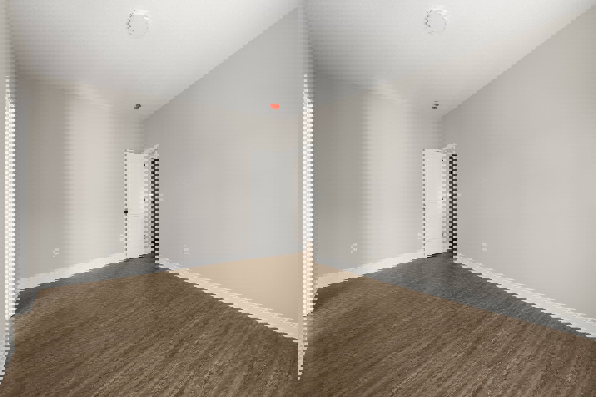 White door with black knob opens into a room with light wood laminate flooring, white plaster walls, and a white circular ceiling light.