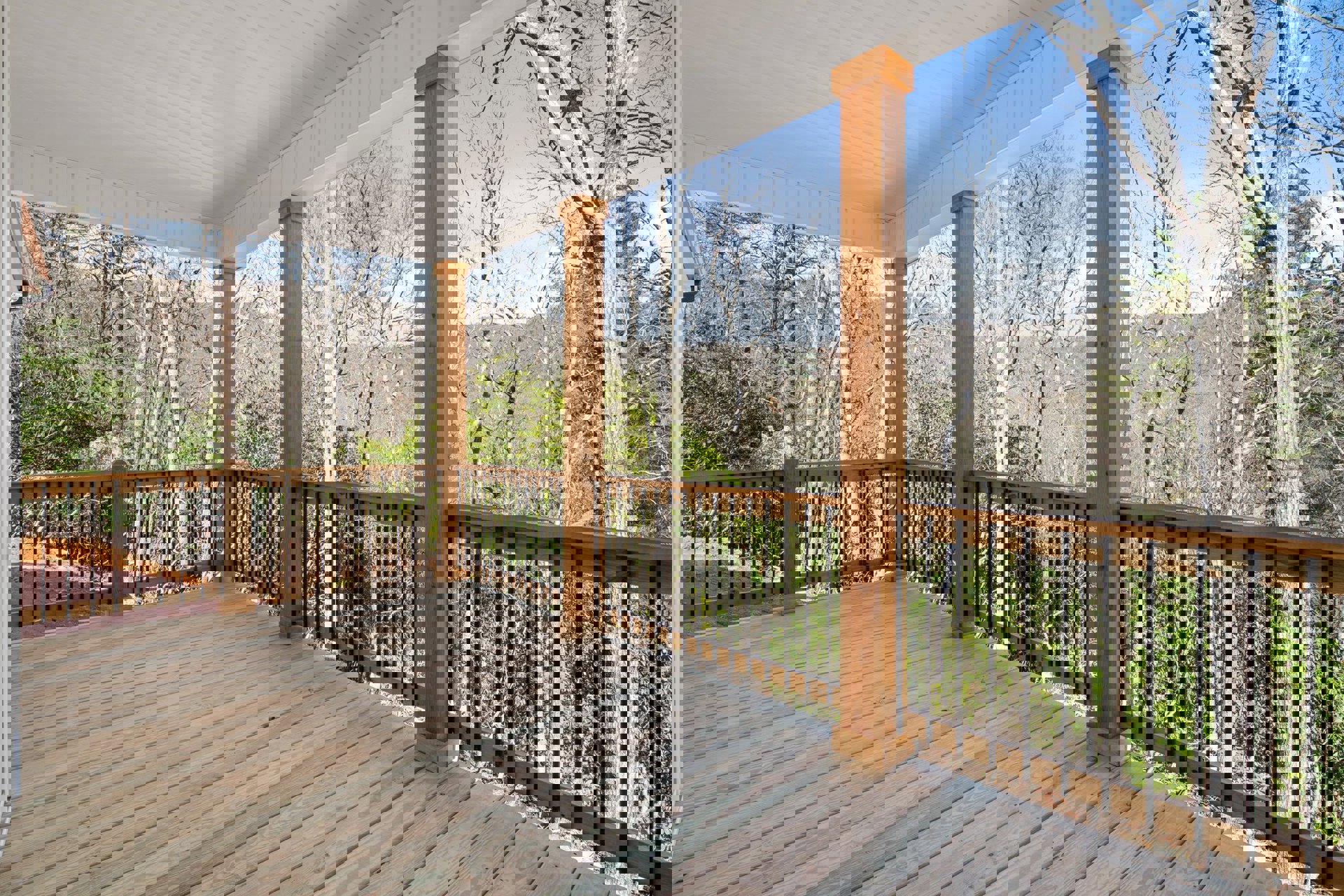 White deck with wooden square post, railing, and view of leafy trees in the background