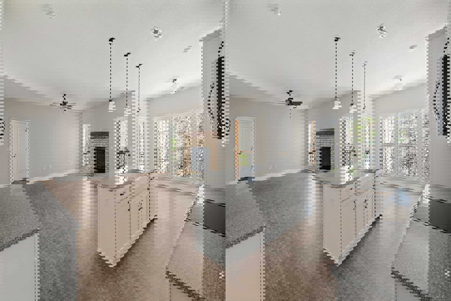 Spacious kitchen featuring a white marble island, built-in fireplace with tile surround, white cabinetry with black handles, large windows overlooking trees, and sleek black