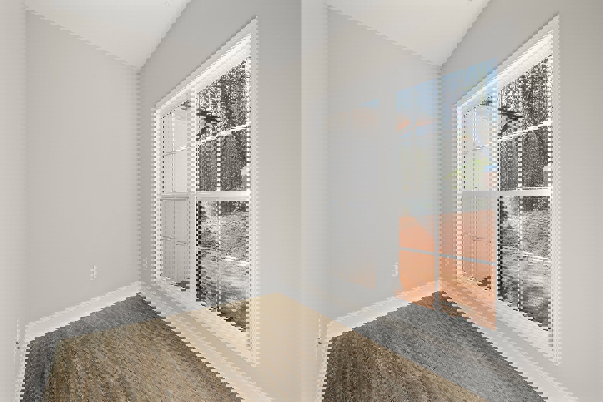 Wood flooring with white trim, large window overlooking dirt field and trees, white walls in a bright interior room