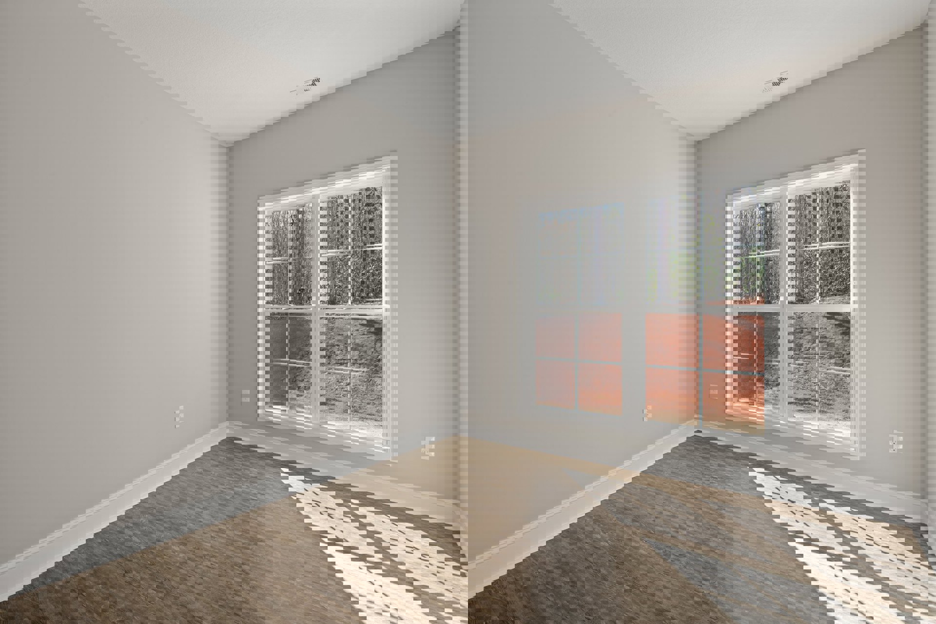 Sunlit wood flooring in a room with plaster walls, large window overlooking forest, and metal floor vent near baseboard