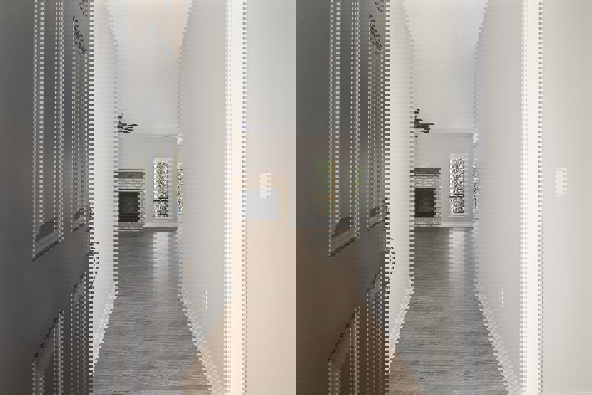 Hallway with wood flooring, white walls, black door, glass-front fireplace with black frame, large window overlooking trees, and white rectangular wall feature