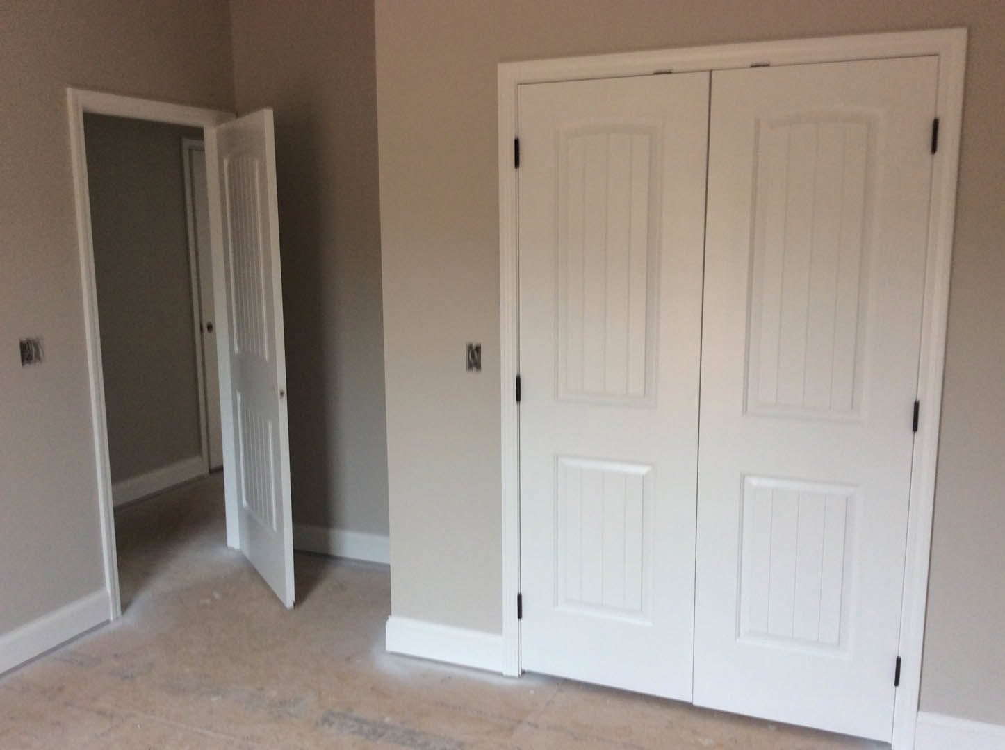 White door with black trim and modern handle, set in a neutral room with wood flooring and white walls