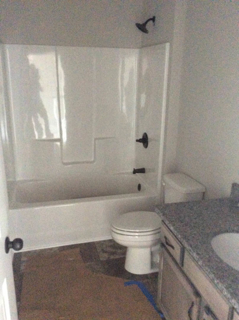 White tile bathroom with black hardware, white toilet, rectangular sink, and partial view of a bathtub.