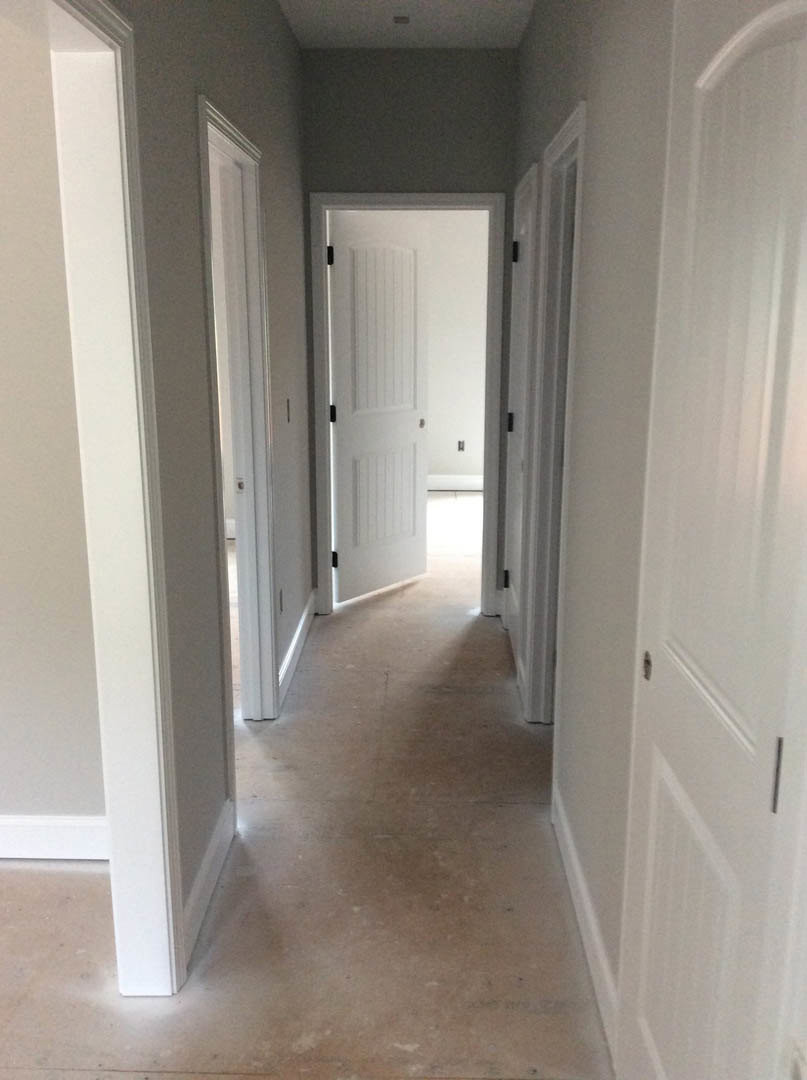 Hallway with white doors, white walls, black handles, and light flooring
