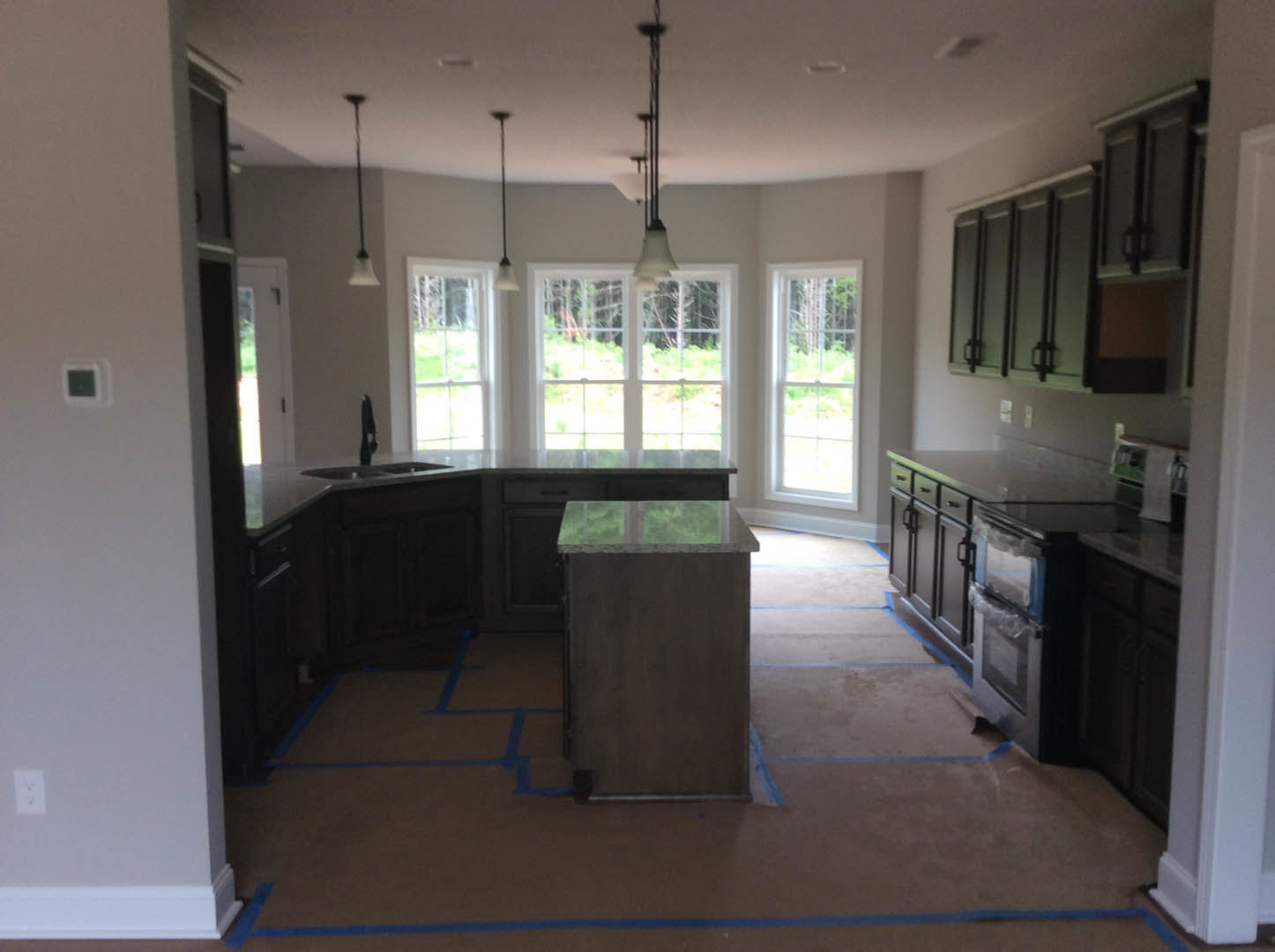 Modern kitchen featuring a central island with brown cabinetry and a green countertop, white walls, large windows providing outdoor views, built-in sink, and light flooring.